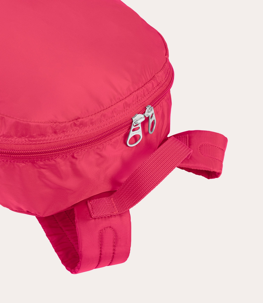 Nahaufnahme einer pinkfarbenen Tasche mit Reißverschluss und Riemen auf weißem Hintergrund.