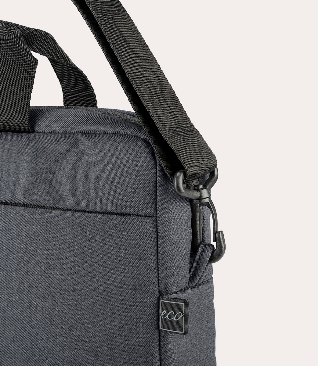 Primo piano di una borsa grigia per laptop. Cinghia e manico neri visibili. Un'etichetta con la scritta 'eco' è attaccata alla borsa.