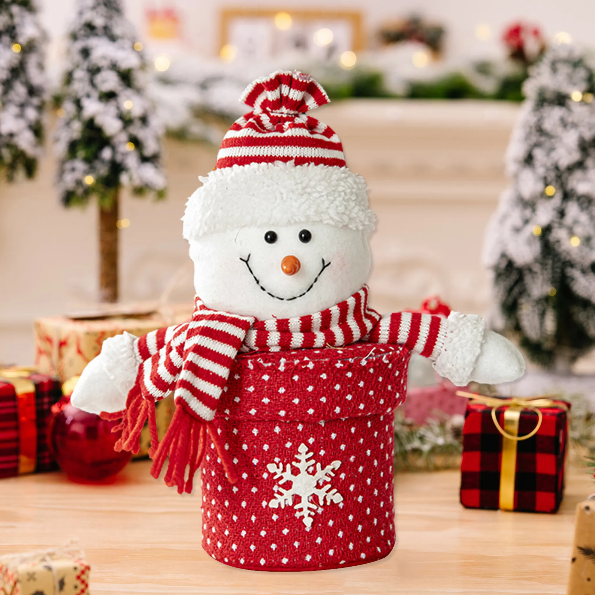 Eine Schneemann-Dekoration mit rot-weiß gestreifter Mütze und Schal vor Weihnachtsdekorationen.