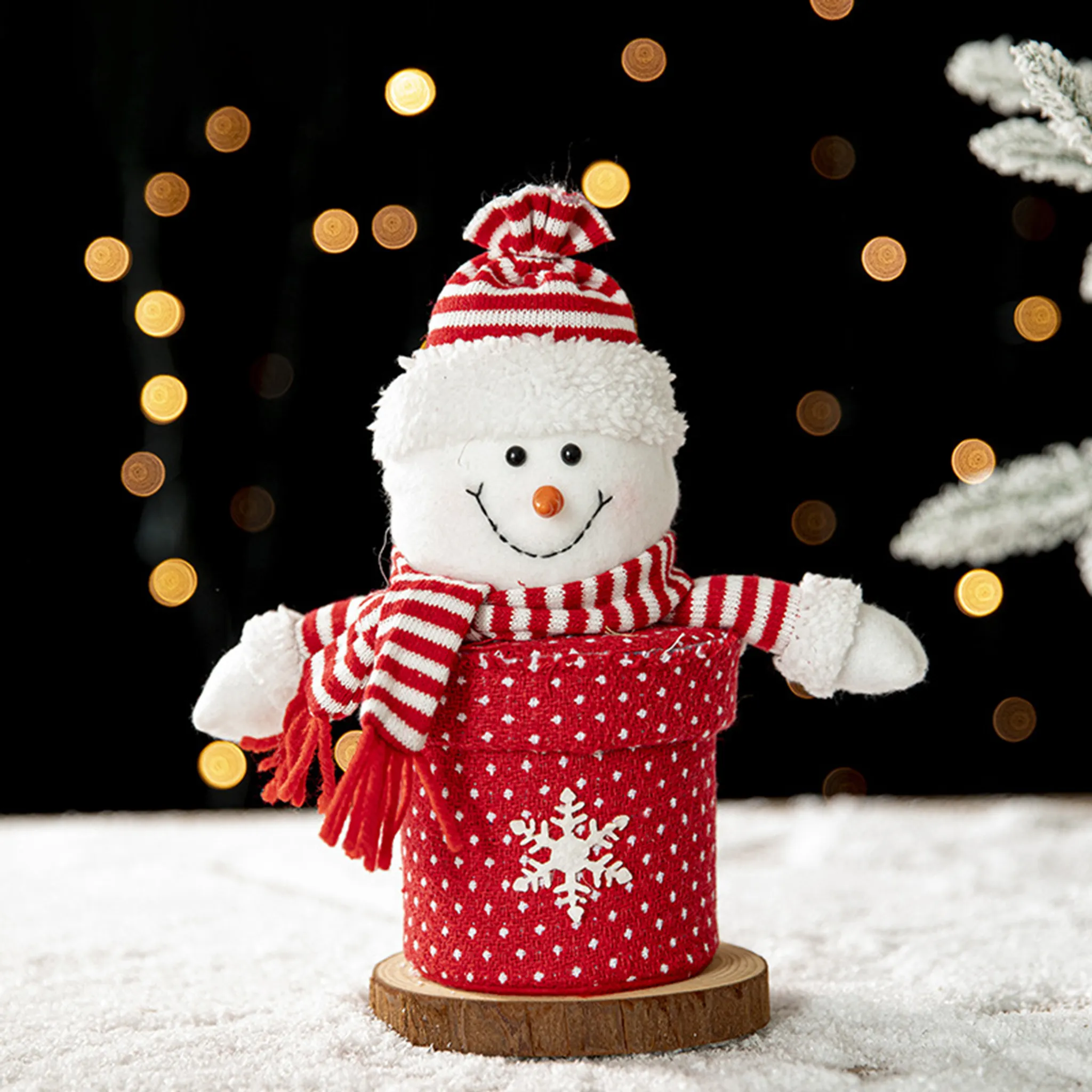 Eine Schneemann-Weihnachtsdekoration. Er hat eine rot-weiße Mütze und einen Schal. Er sitzt auf einem Holzsockel.
