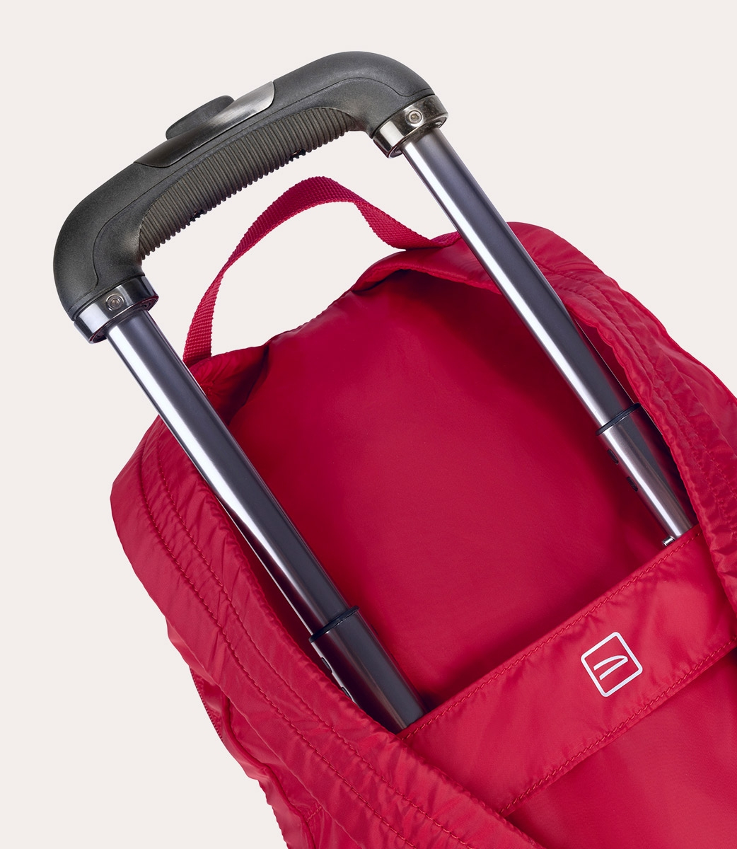 Rote Reisetasche mit schwarzem Griff und silbernen Metallstangen. Die Tasche hat einen kleinen Griff und ein weißes Logo.