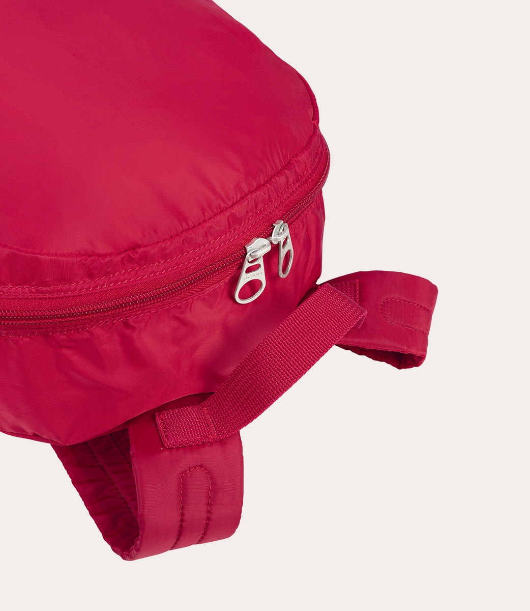 Nahaufnahme eines roten Rucksacks. Der Reißverschluss ist geöffnet, und ein Gurt erstreckt sich nach rechts. Weißer Hintergrund.