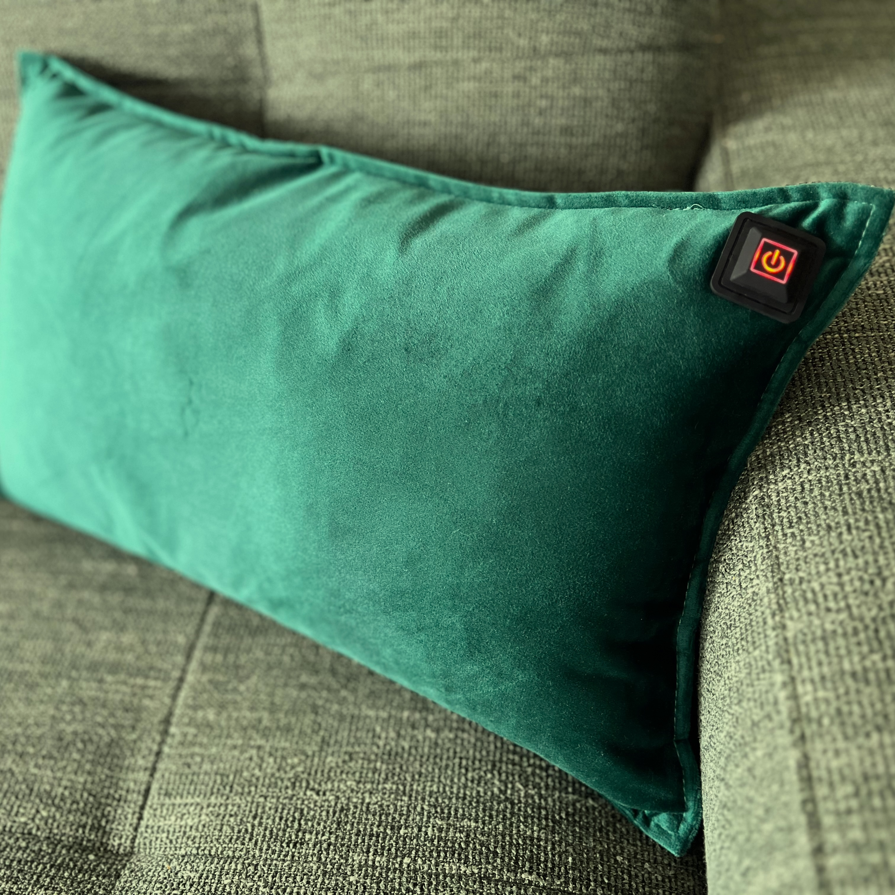 Ein grünes Samtkissen mit einem Einschaltknopf liegt auf einem grün strukturierten Sofa.