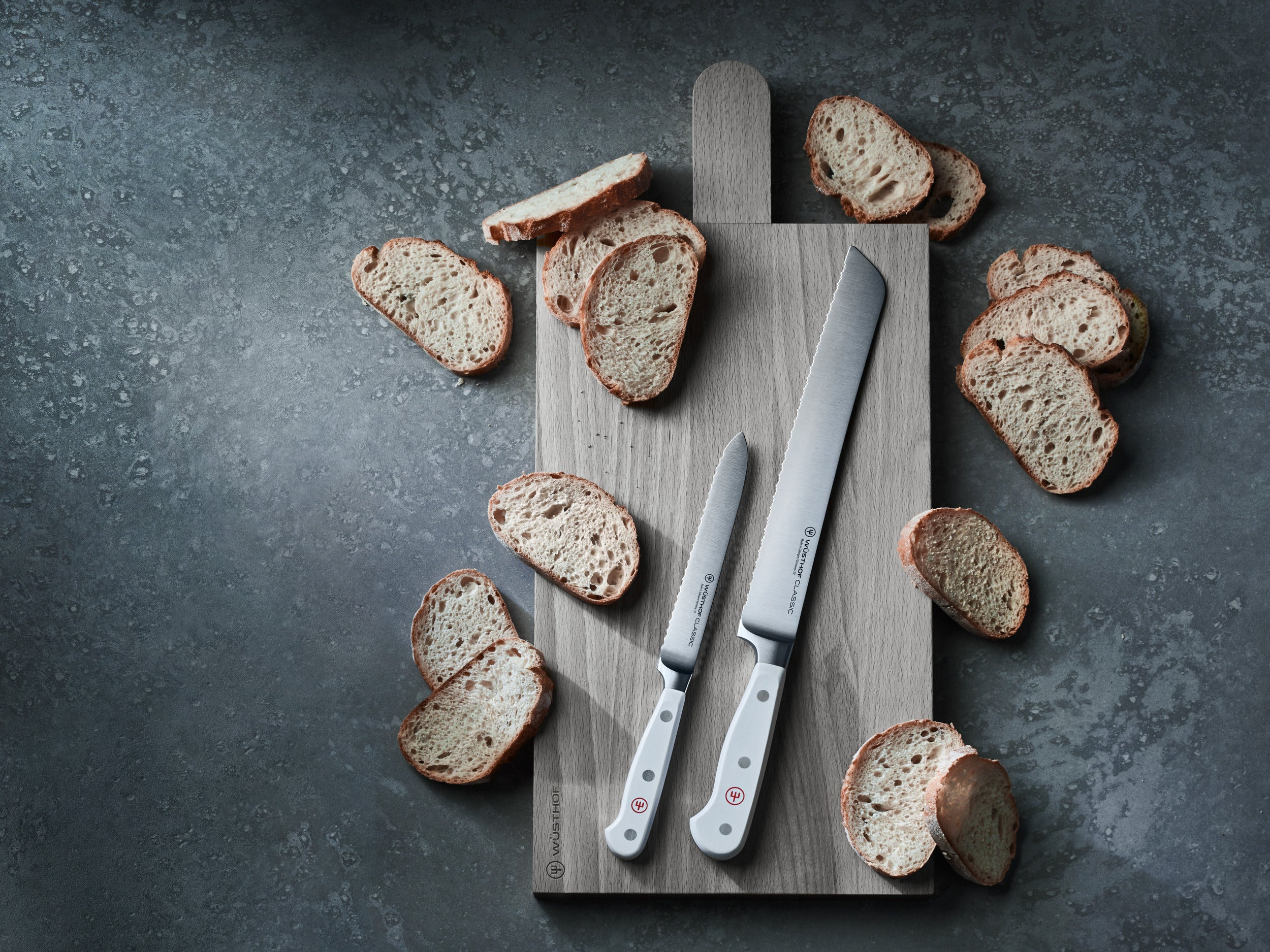 Brotscheiben, zwei Messer und ein Schneidebrett, auf grauem Hintergrund angeordnet.