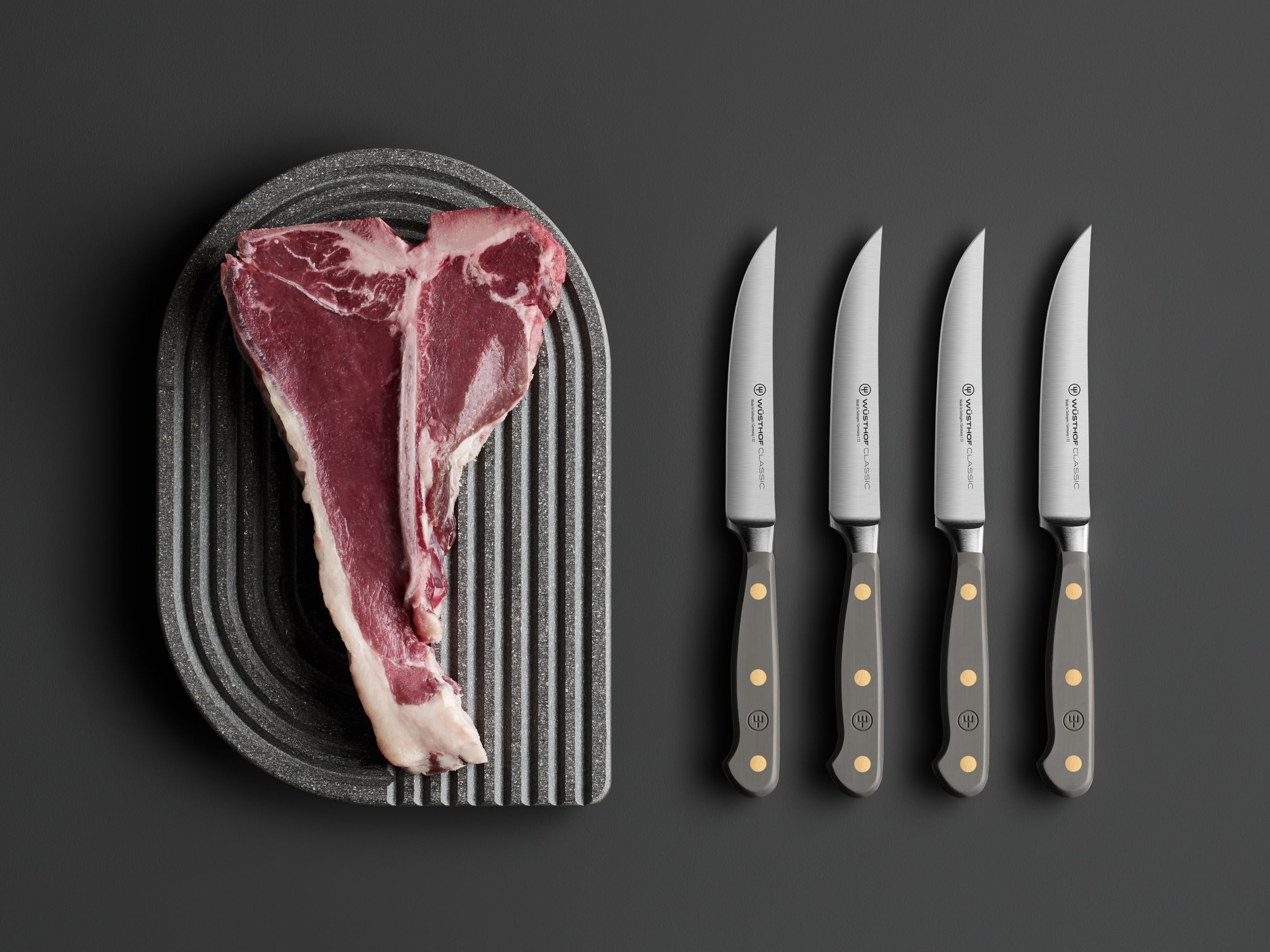 Ein T-Bone-Steak auf einem strukturierten Teller mit vier Messern auf grauer Oberfläche.