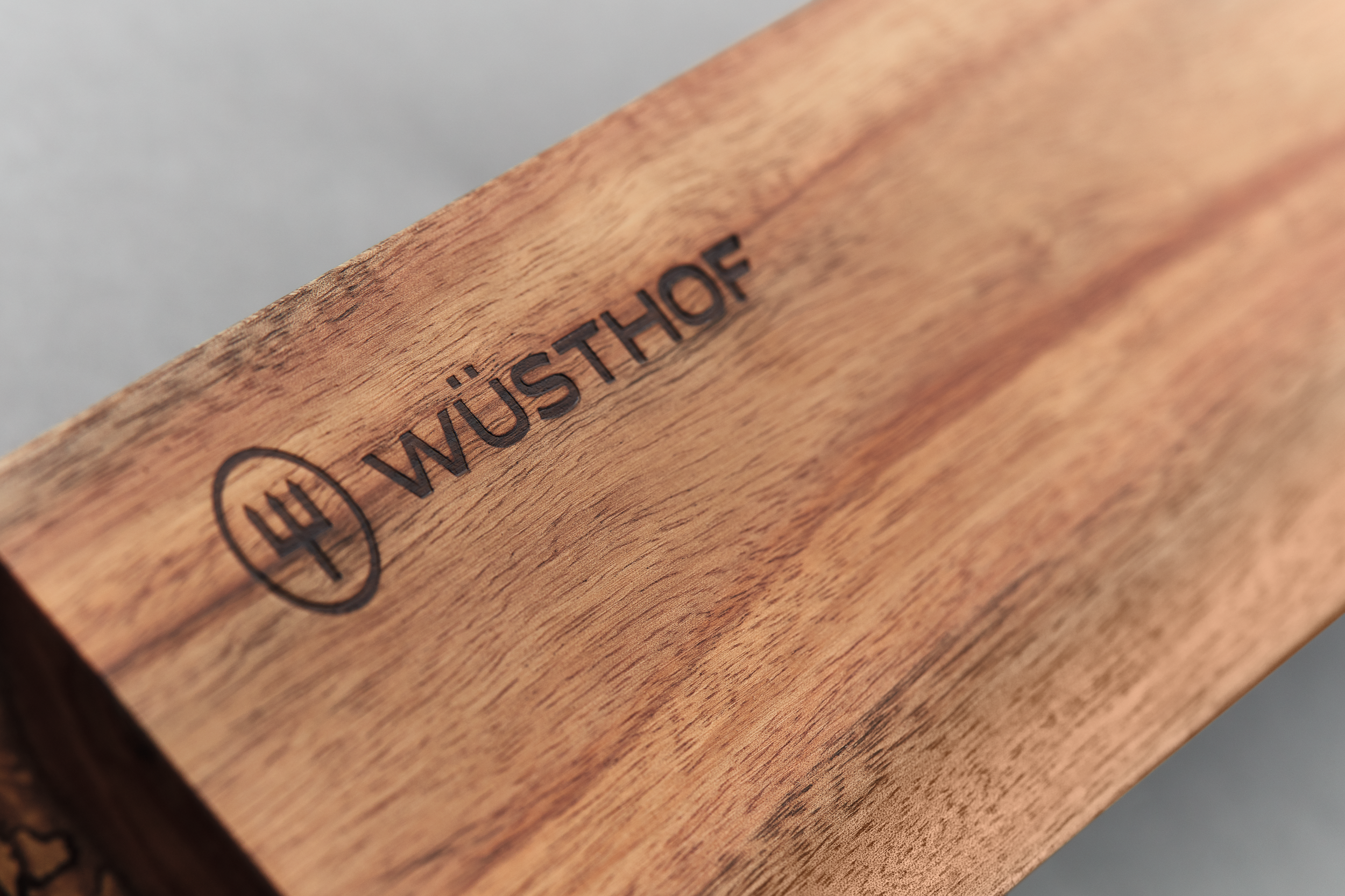 Nahaufnahme eines Holzschneidebretts mit dem WÜSTHOF-Logo und einem Dreizack-Symbol. Das Holz hat eine natürliche Maserung.