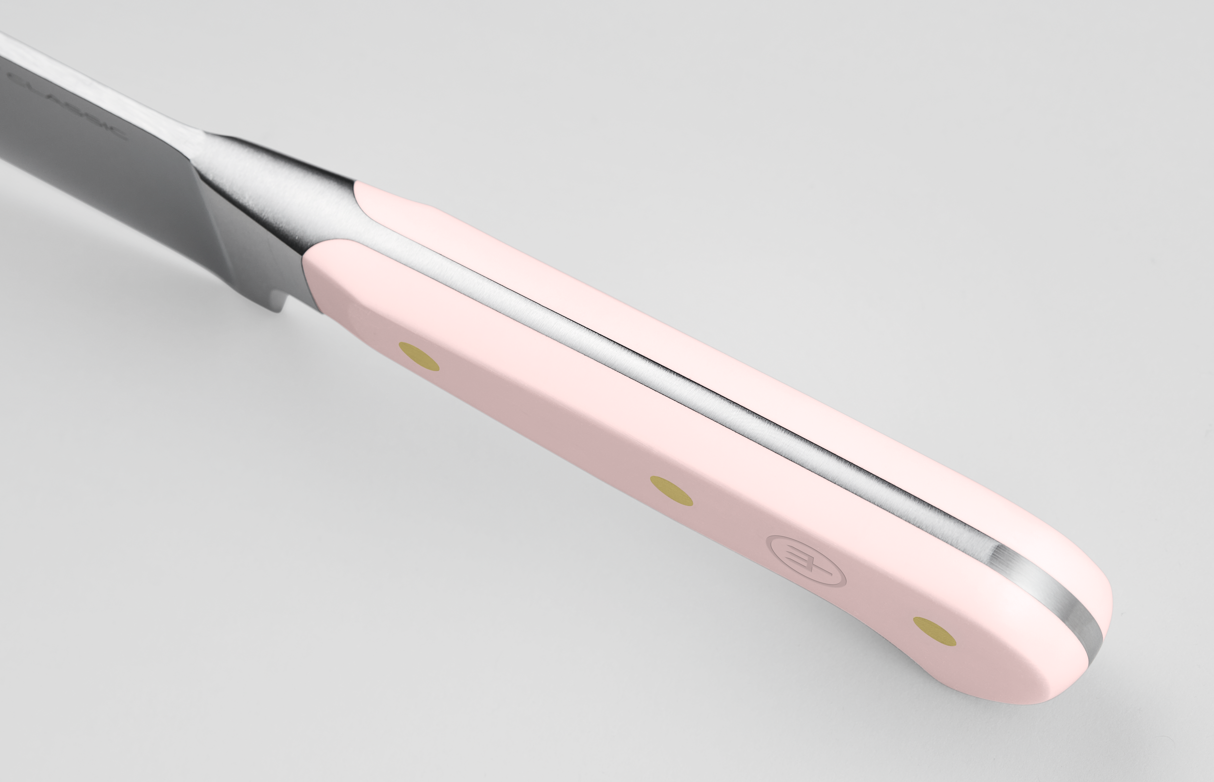 Nahaufnahme eines Messers. Der Griff ist rosa mit goldenen Nieten. Die Klinge ist silberfarben und scharf. Der Hintergrund ist weiß.