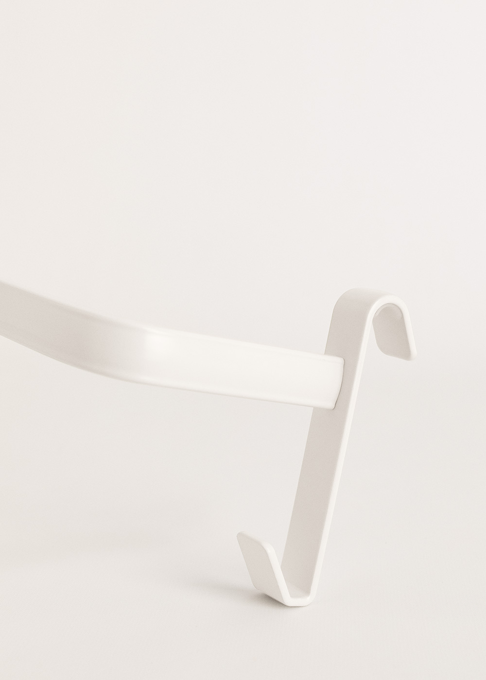 Un gancho de metal blanco, diseñado para colgar sobre una puerta o estructura similar, sobre un fondo blanco.