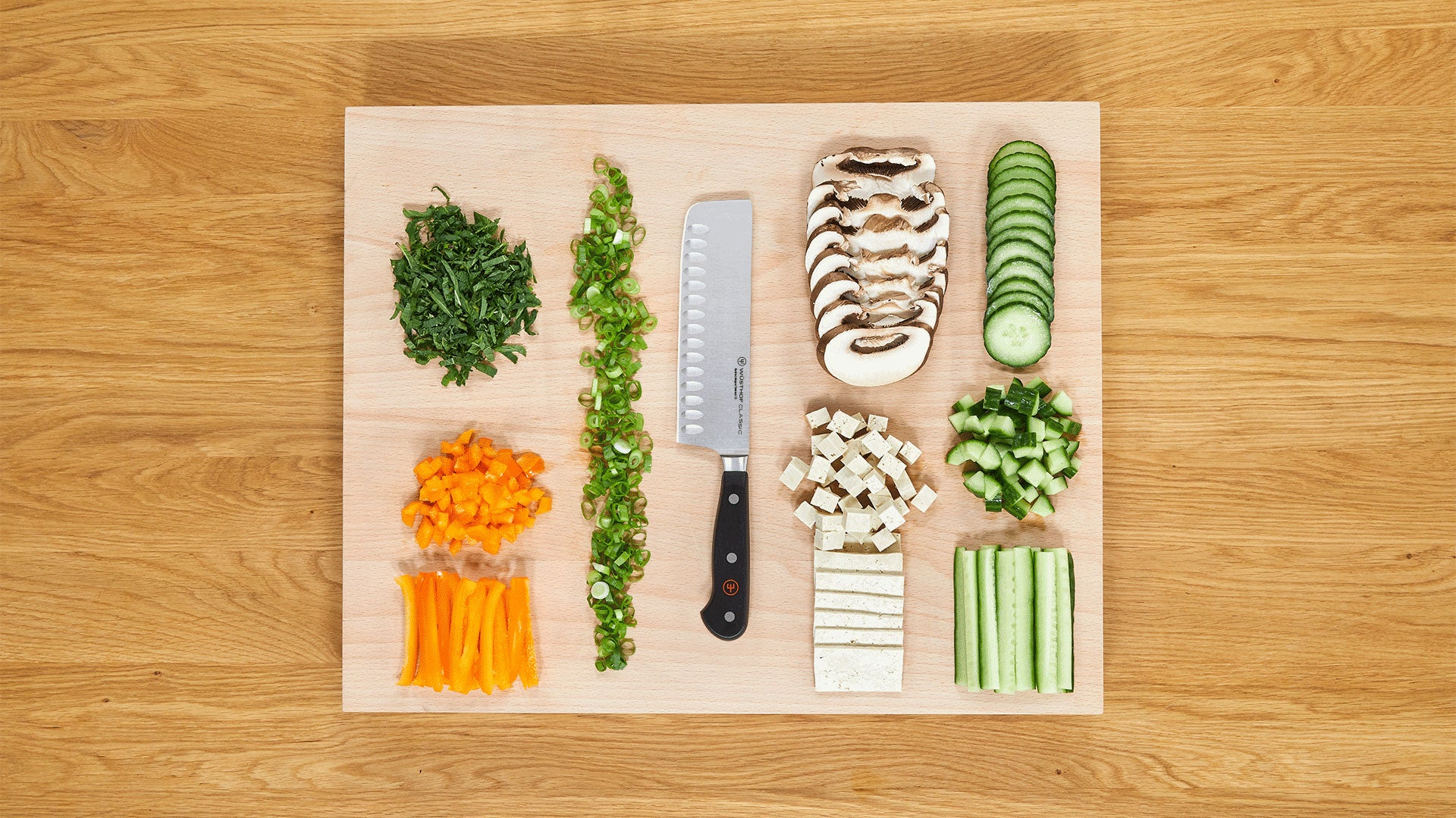 Ein Holzzchneidebrett mit verschiedenem gehacktem Gemüse und einem Messer. Enthält Grünzeug, Karotten, Pilze, Tofu und Gurken.