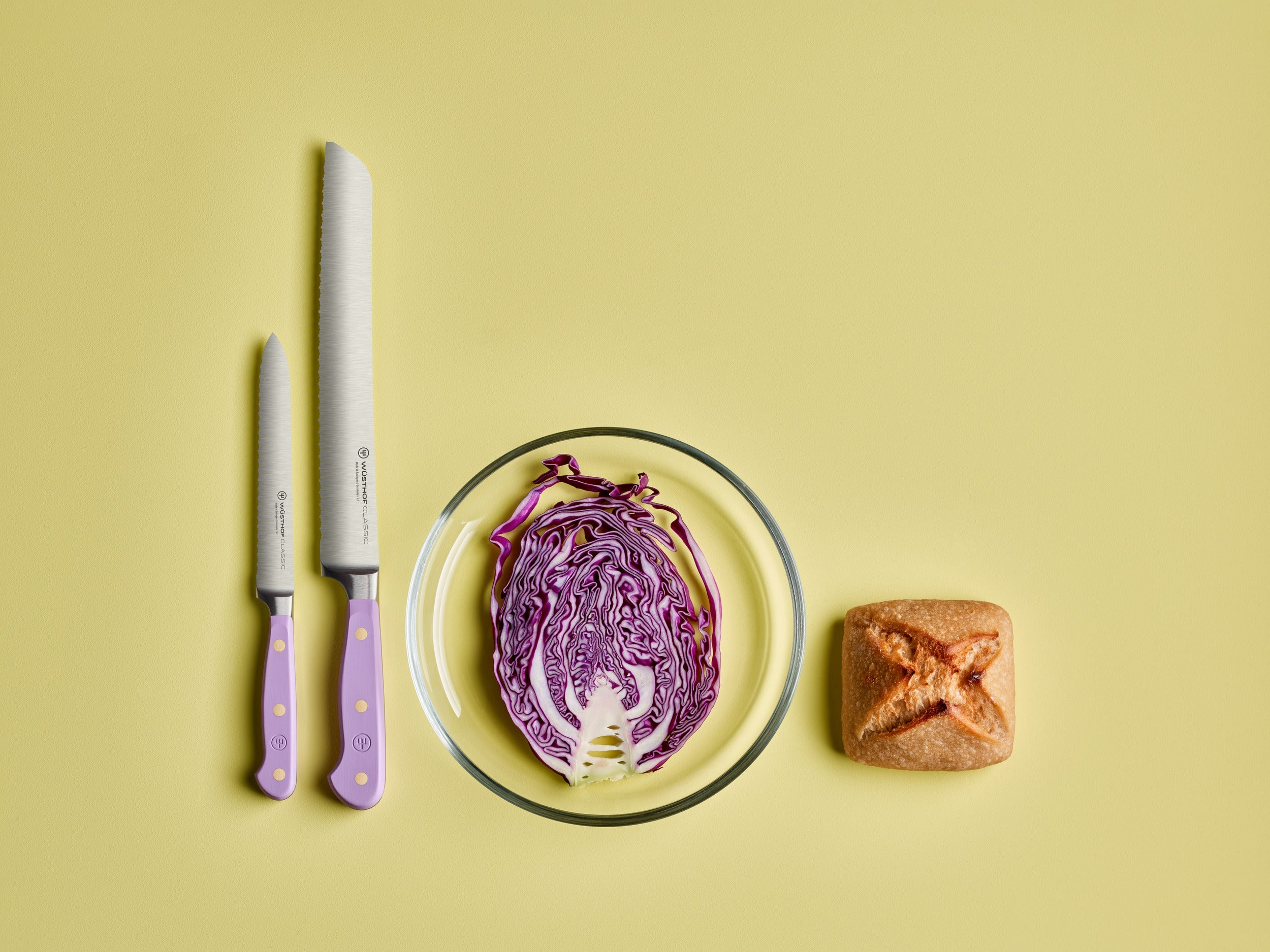 Ein gelber Hintergrund mit zwei Messern, Rotkohl in einer Glasschale und Brot.