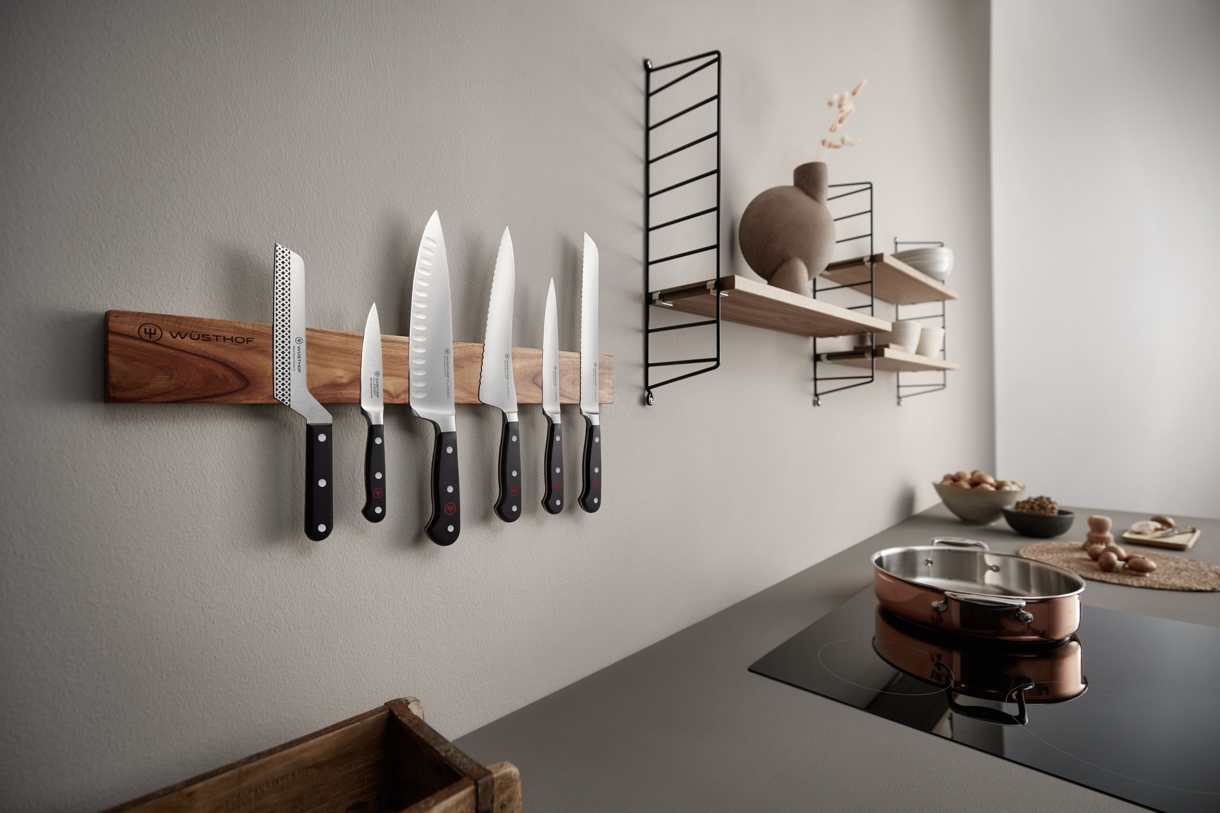 Küchenszene mit Messern an der Wand, Regalen und einem Herd. Kupferpfanne auf der Theke mit Lebensmitteln.