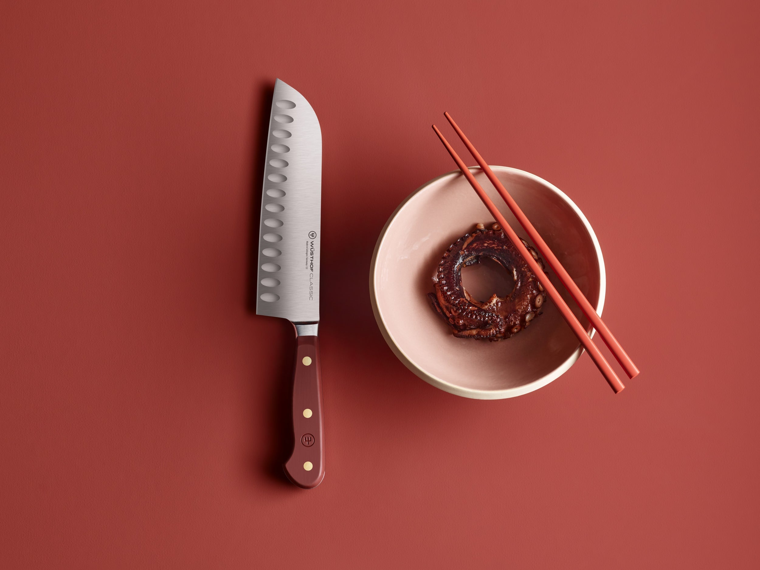 Ein Messer und eine Schüssel mit Essen und Essstäbchen auf roter Oberfläche.