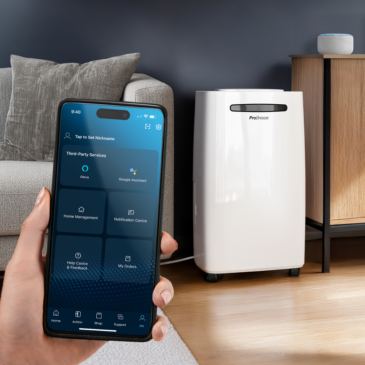 Eine Hand, die ein Telefon mit einer Smart-Home-App hält. Ein weißer Luftentfeuchter und ein Holzschrank sind im Hintergrund.