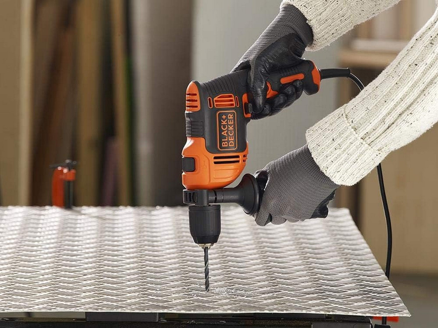 Una persona sta usando un trapano Black+Decker per forare una rete metallica. Il trapano è arancione e nero.