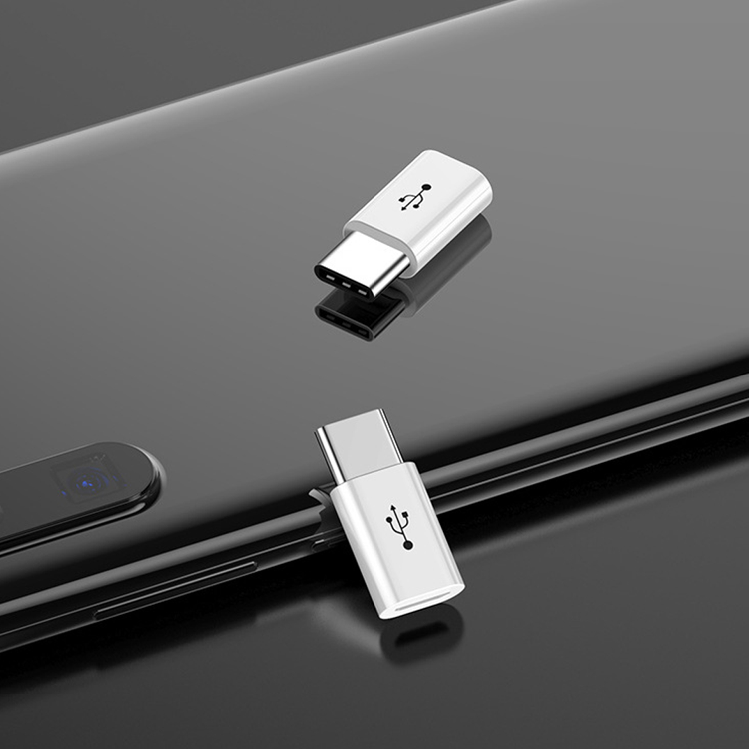 Zwei weiße USB-C-Adapter mit USB-Symbolen auf einer schwarzen, reflektierenden Oberfläche. Einer liegt über dem anderen mit Spiegelung.