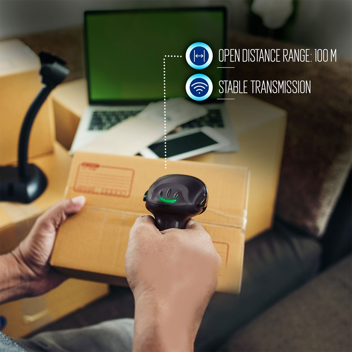 Una persona scansiona una scatola di cartone con uno scanner di codici a barre. Un laptop e un telefono sono sullo sfondo, insieme al testo sulla portata e sulla trasmissione.
