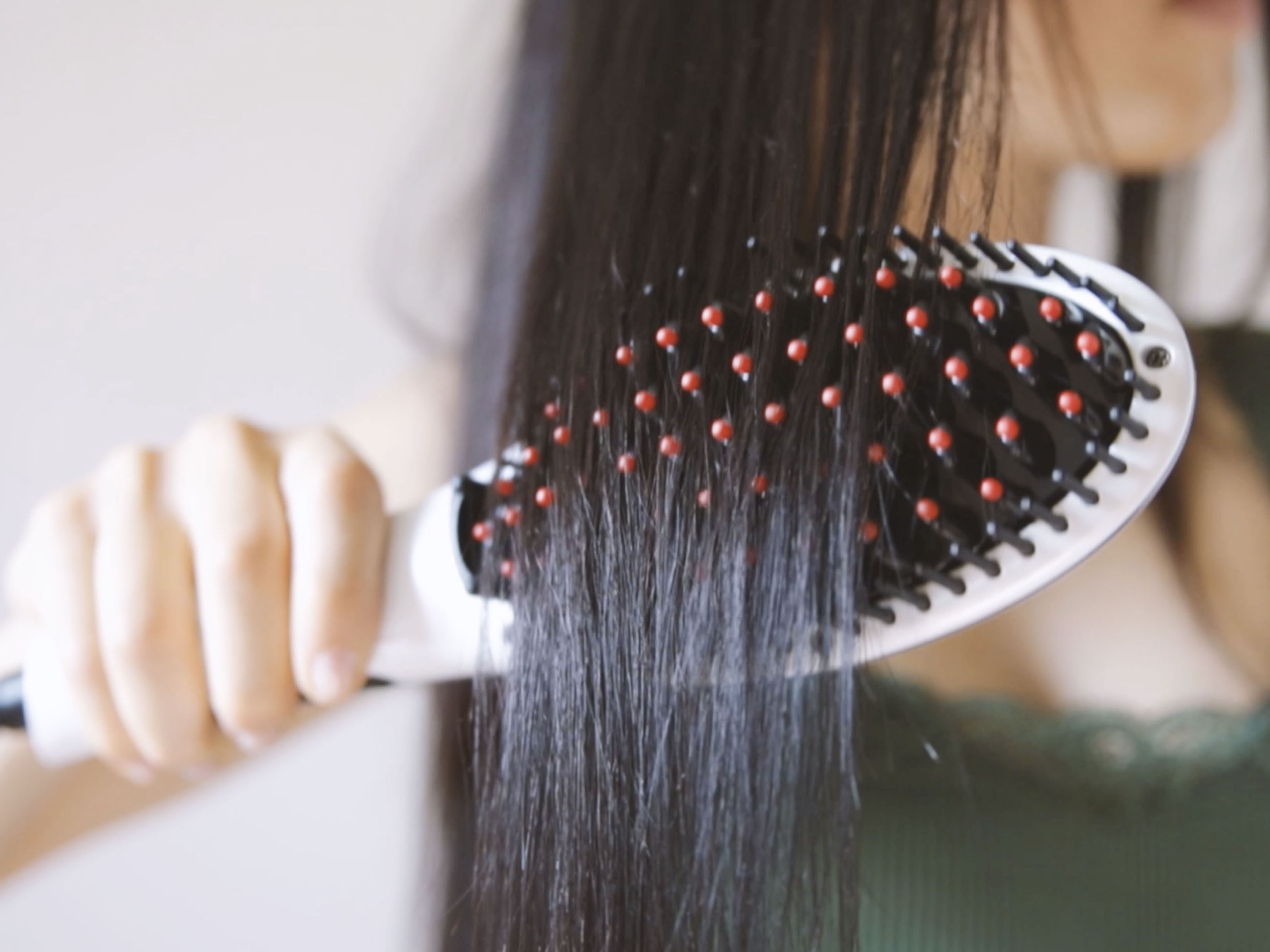 Una persona spazzola capelli lunghi e scuri con una spazzola bianca e nera con punte rosse.