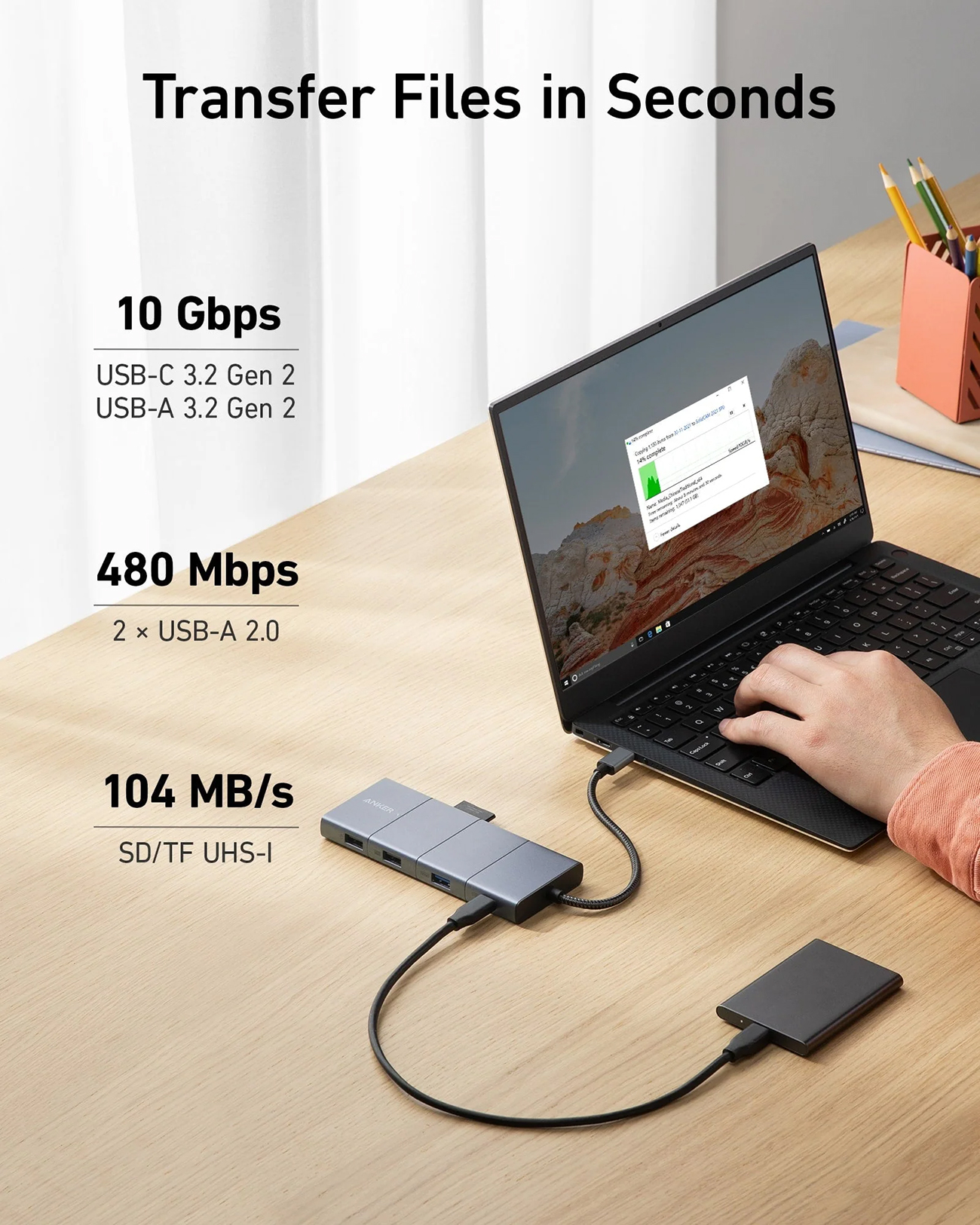 Un laptop è collegato a un hub e a un disco rigido esterno. Lo schermo del laptop mostra un trasferimento di file. Le velocità di trasferimento dati sono elencate.