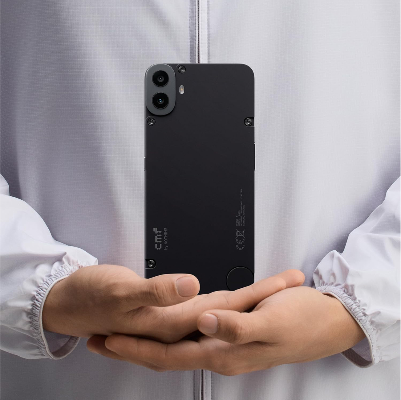 Eine Person hält ein schwarzes Smartphone. Das Telefon hat zwei Kameras und das CMF by Nothing Logo. Der Hintergrund ist eine weiße Jacke.
