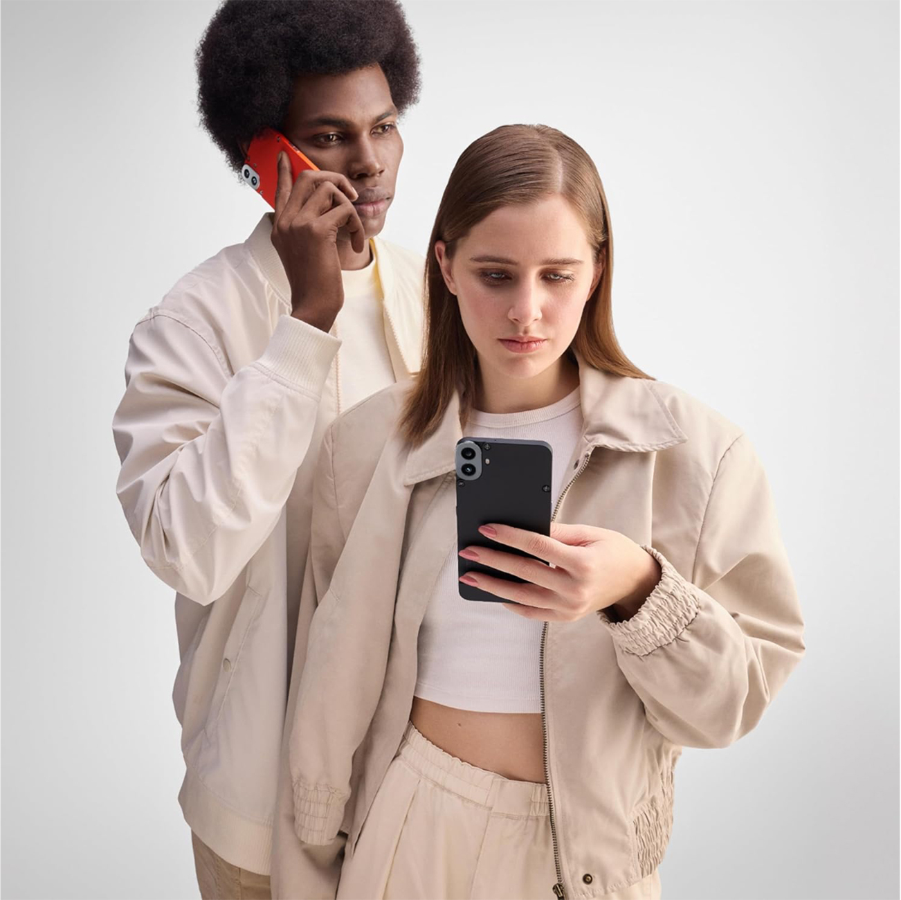 Zwei Personen schauen auf Handys. Einer telefoniert mit einem roten Telefon, der andere hält ein schwarzes Telefon.