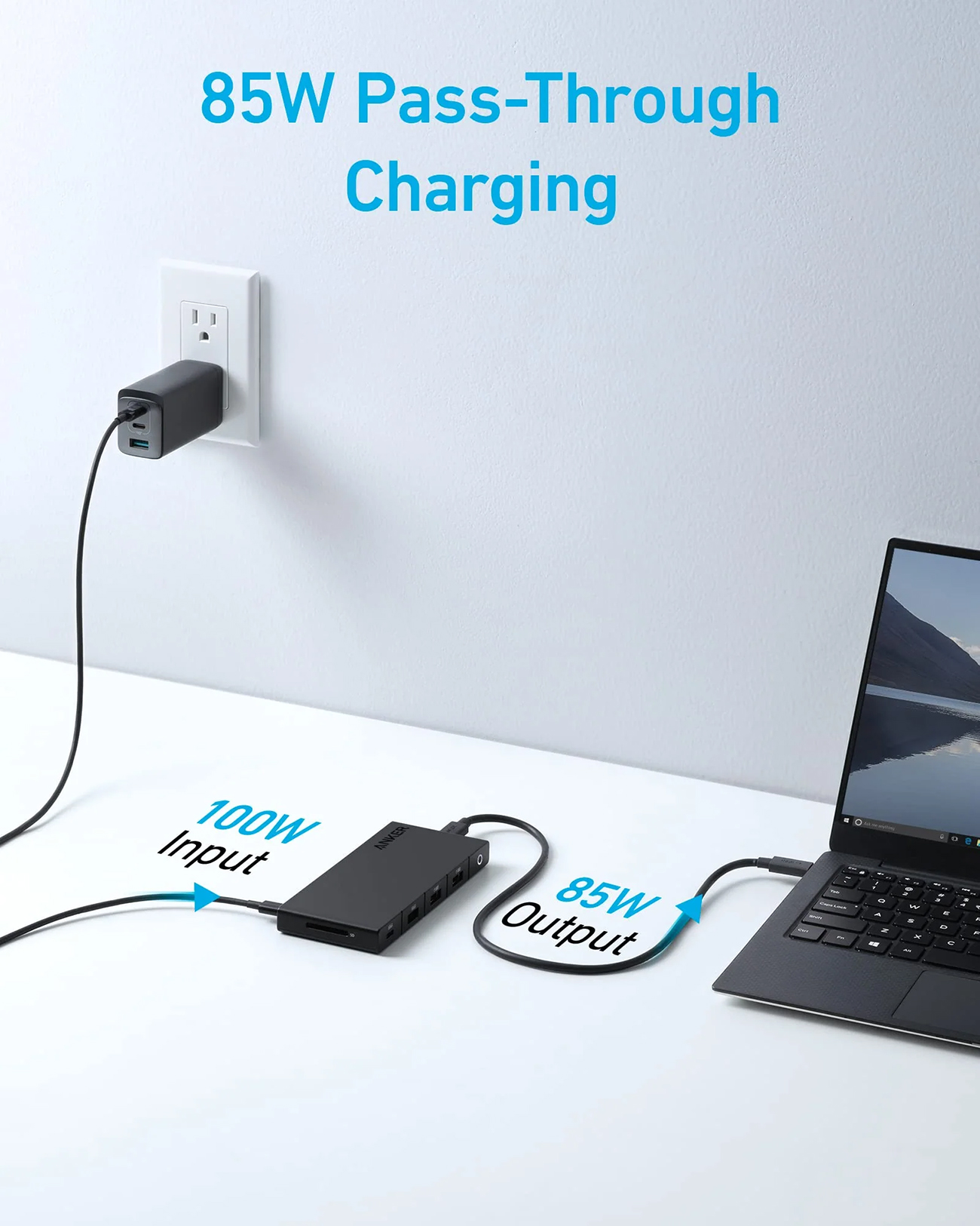 Caricatore nero collegato a una presa a muro, collegato a un laptop e a un hub nero su una superficie bianca, che mostra la ricarica passante a 85W.