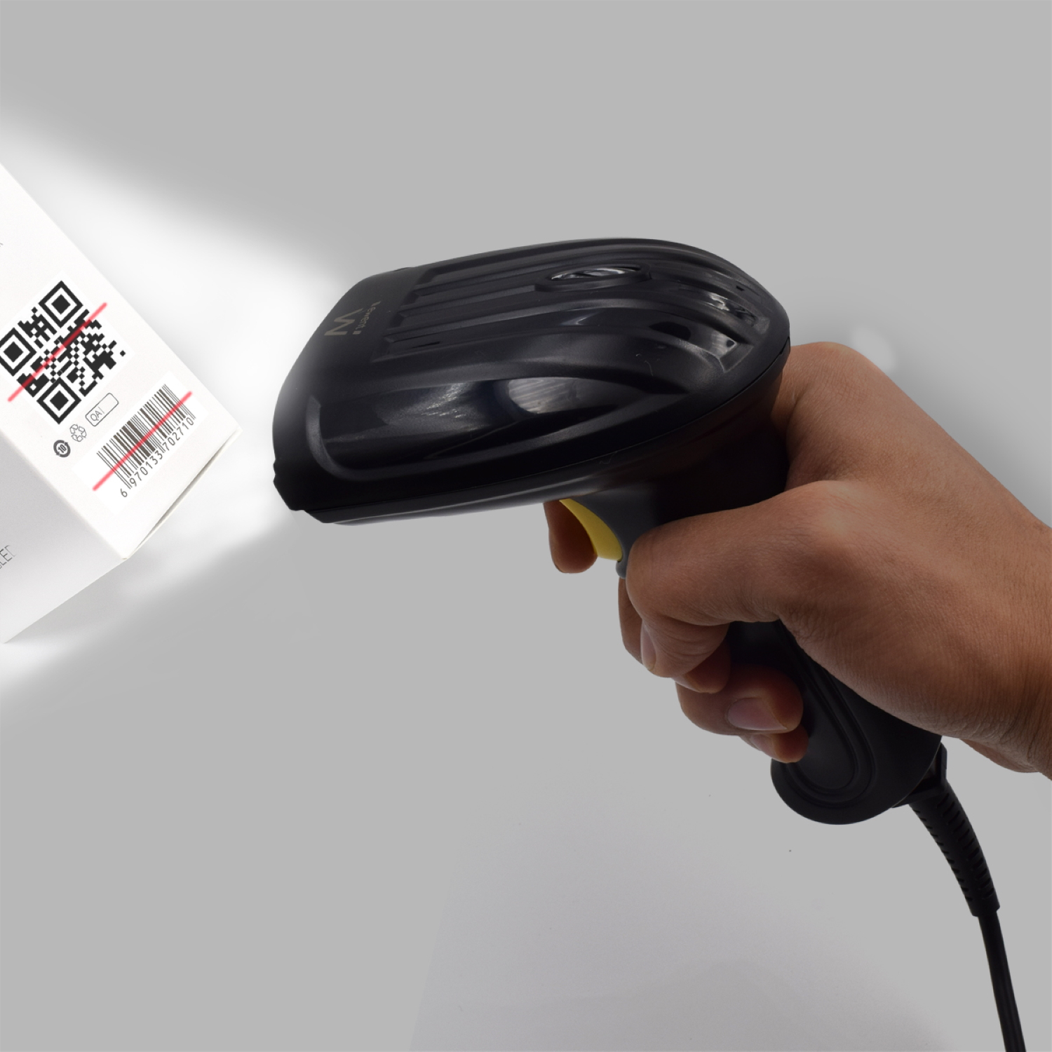 Mano che tiene uno scanner di codici a barre nero puntato verso una scatola bianca con un codice a barre. La scatola ha una linea rossa.