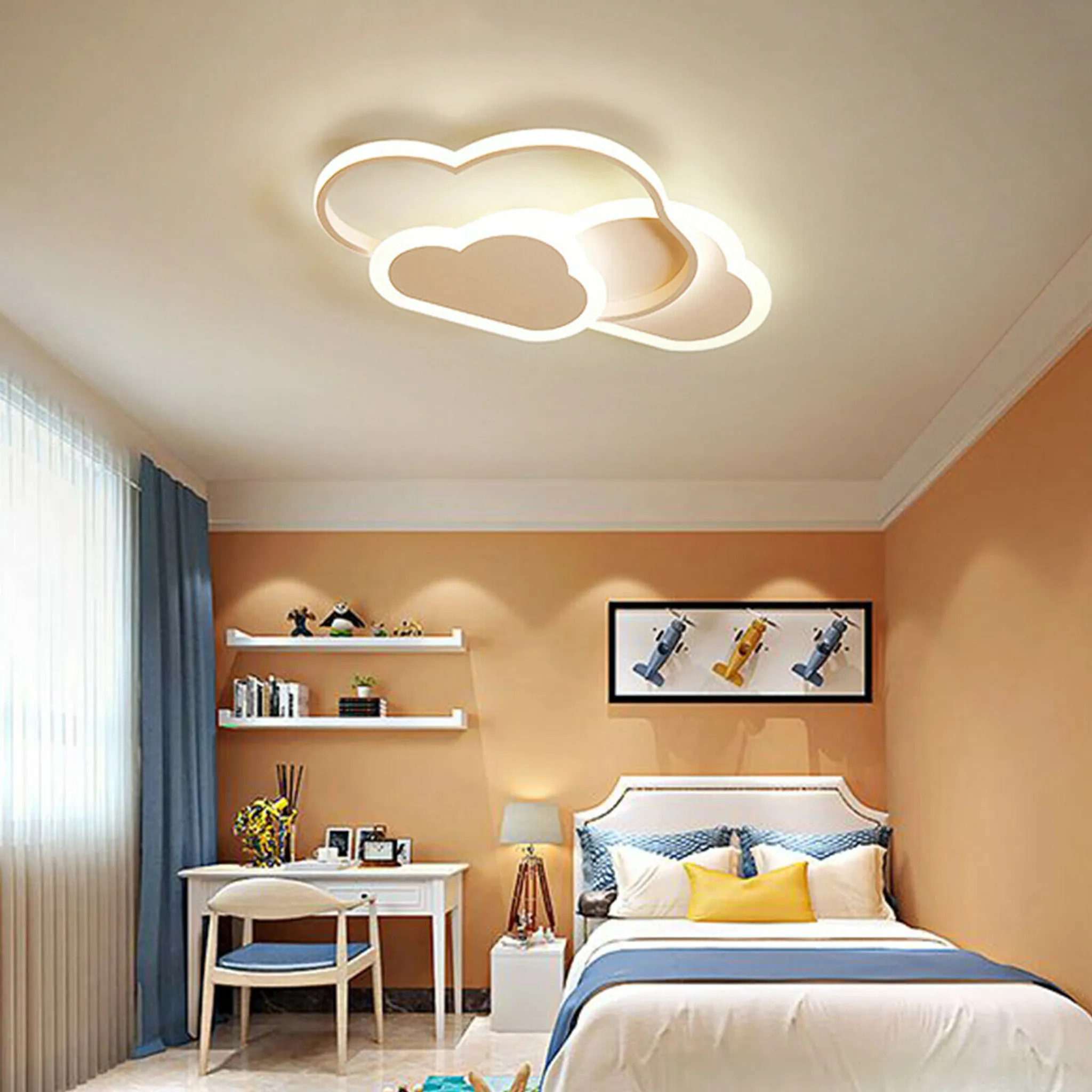 Ein Schlafzimmer mit wolkenförmiger Deckenleuchte, Bett, Schreibtisch, Regalen und einem Bild von Flugzeugen. Farbschema ist Creme und Orange.