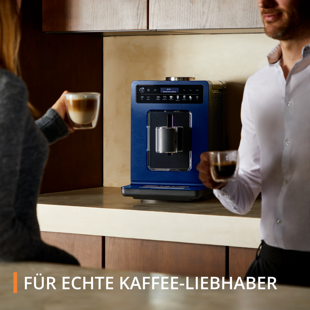 Due persone tengono tazze di caffè vicino a una macchina da caffè blu. Uno tiene un latte, l'altro un espresso. Il testo dice: Per i veri amanti del caffè.