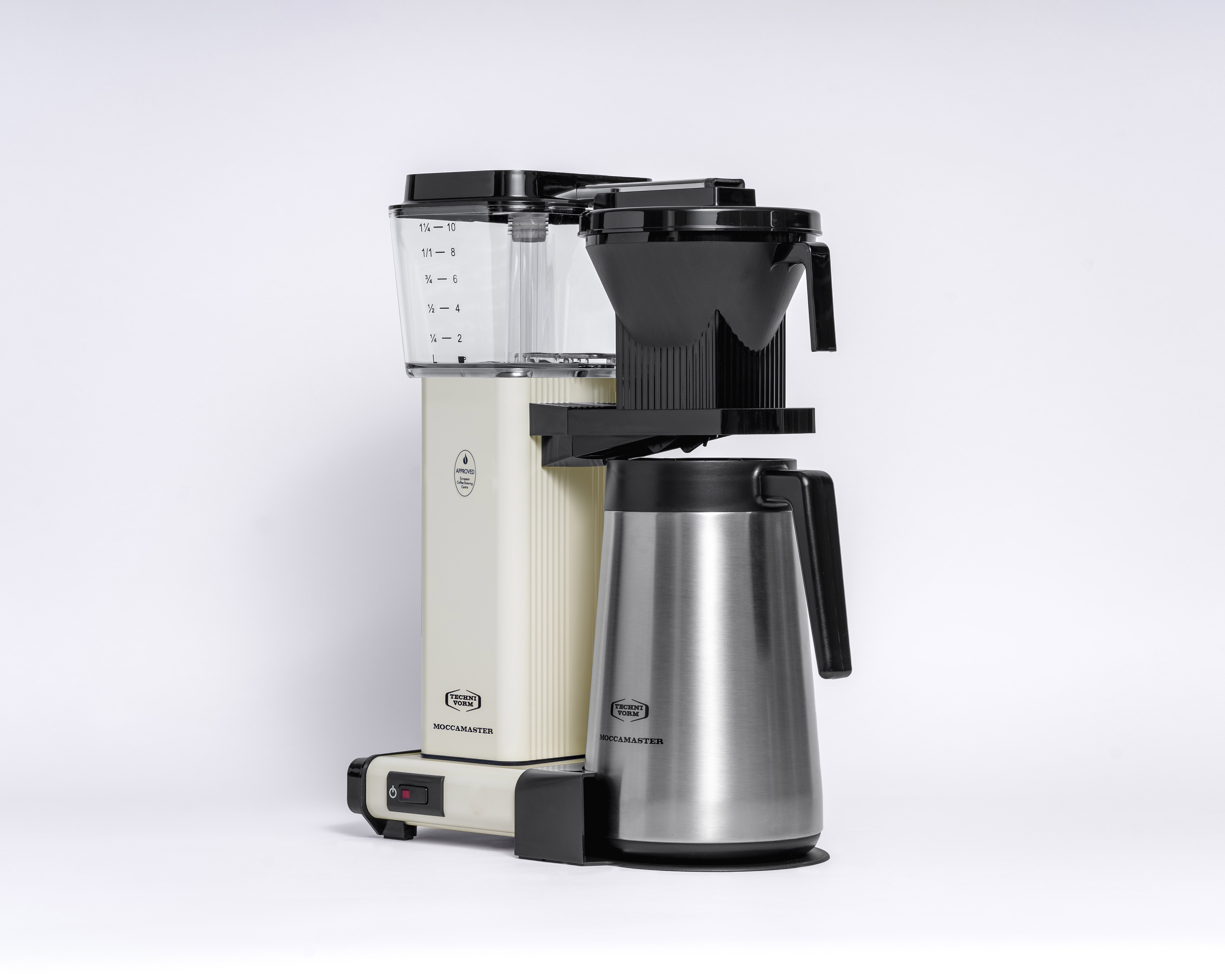 Una caffettiera color crema e nera con una caraffa in acciaio inossidabile. Ha un indicatore del livello dell'acqua e il logo Moccamaster.
