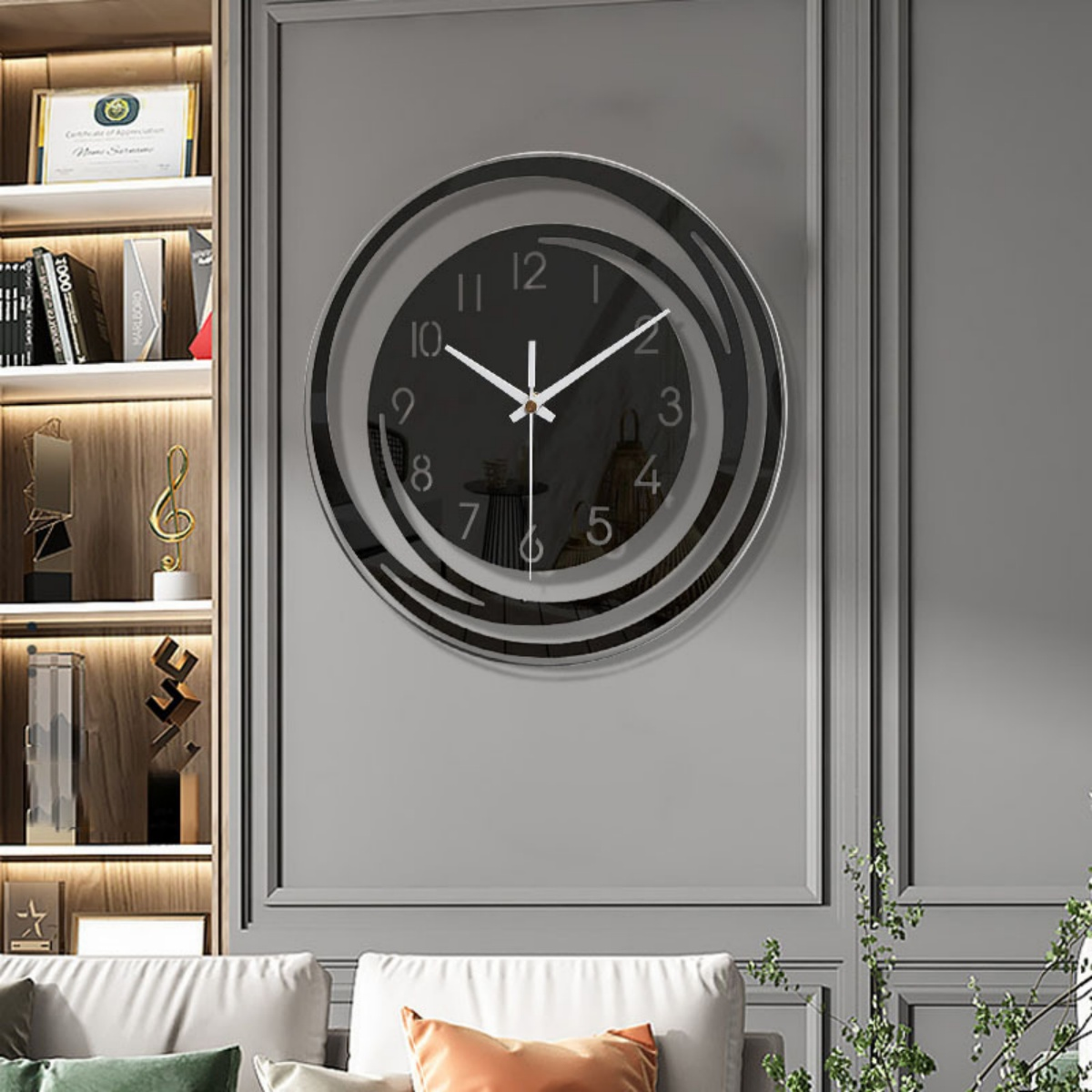 Eine moderne Wanduhr mit schwarzem Zifferblatt und weißen Zeigern hängt an einer grauen Wand über einem weißen Sofa. Links ist ein Bücherregal.