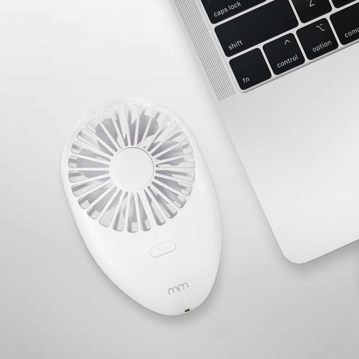 A white handheld fan next to a laptop keyboard on a white surface. The fan has an on/off button and the brand name.