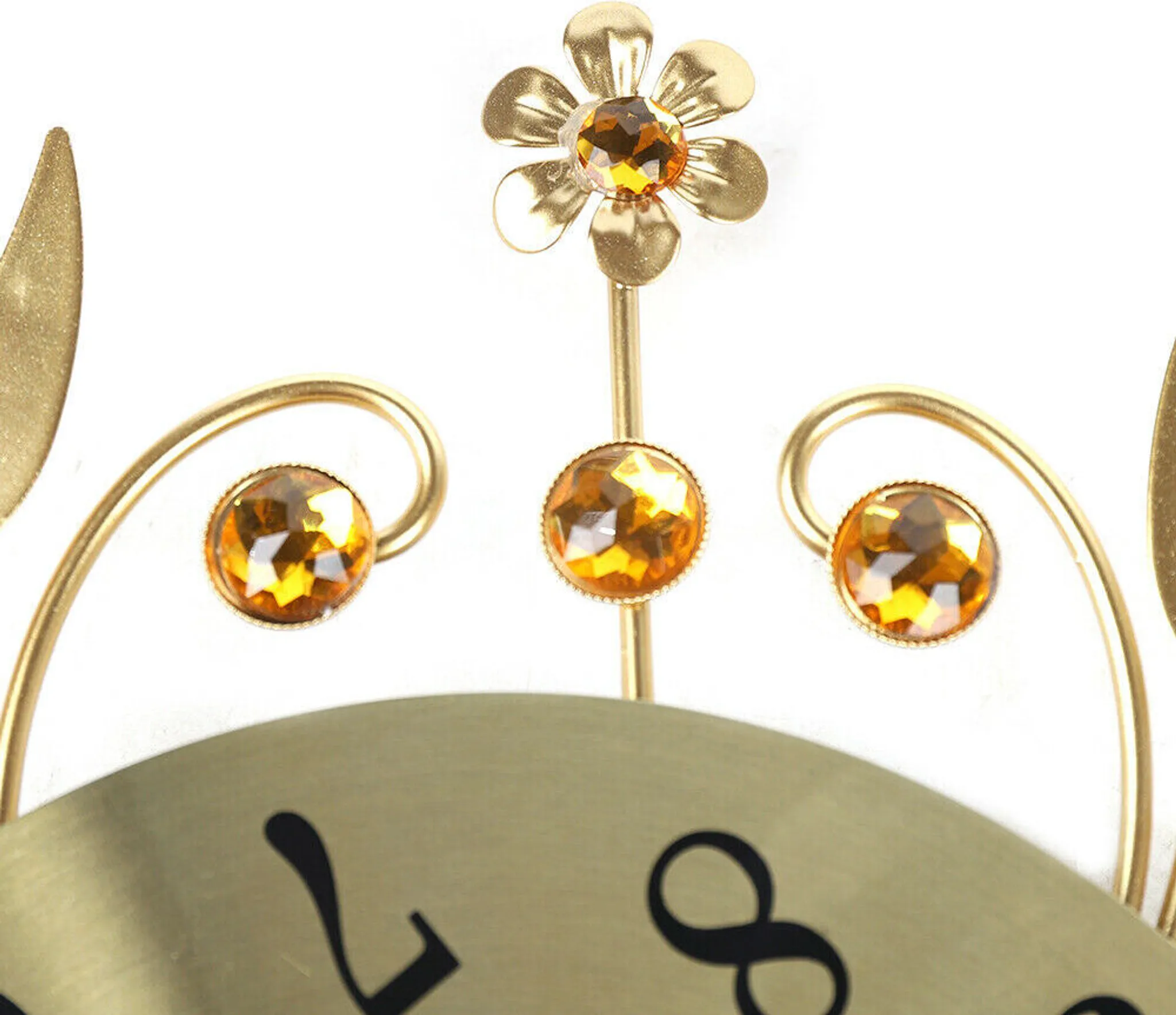 Nahaufnahme einer Uhr mit goldenen Akzenten und orangefarbenen Edelsteinen. Eine Blume und drei Edelsteine sind sichtbar. Weißer Hintergrund.