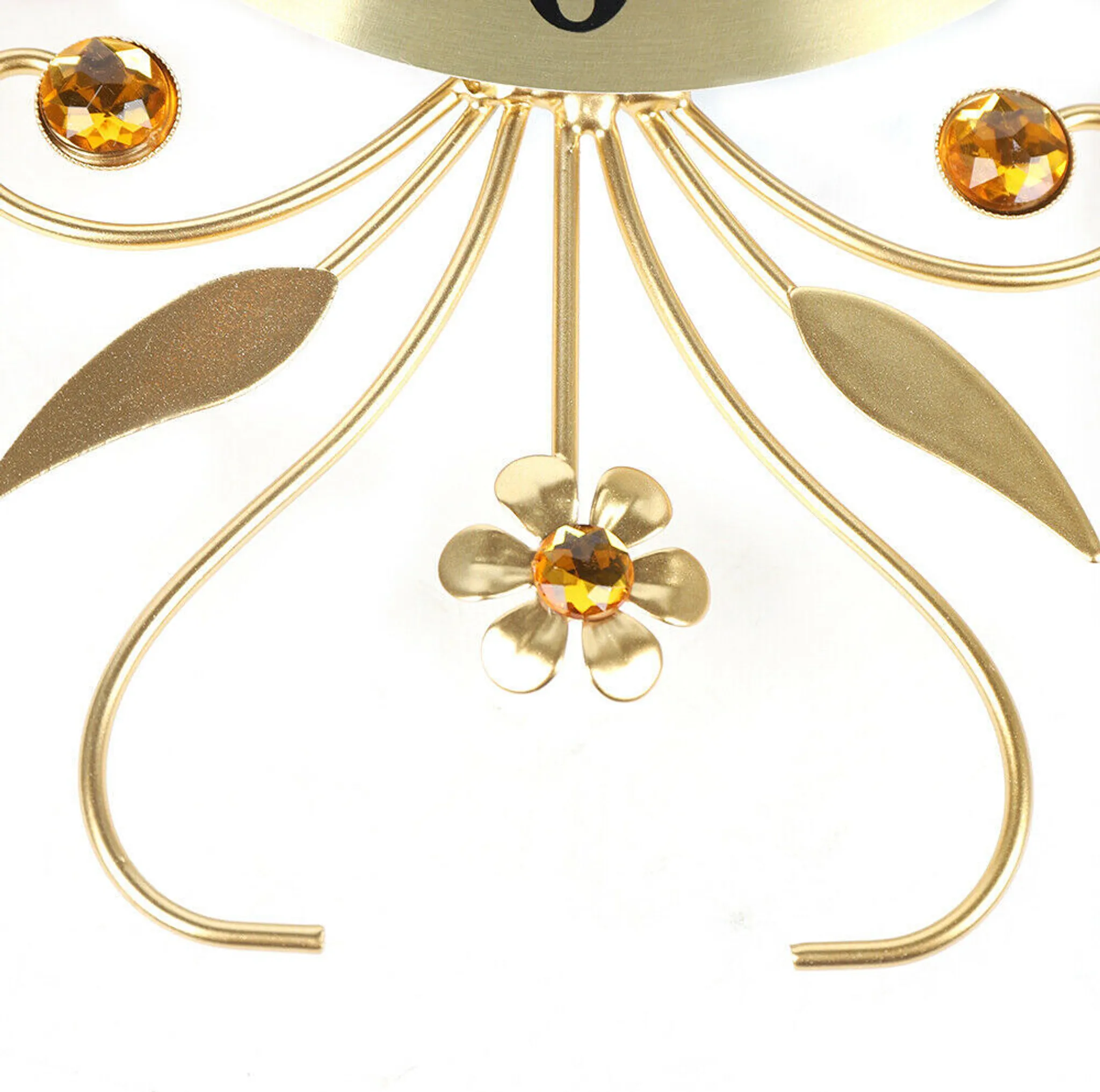 Nahaufnahme eines goldenen Uhrdetails. Aufwendiges Design mit Edelsteinen und Blättern. Heller Hintergrund.
