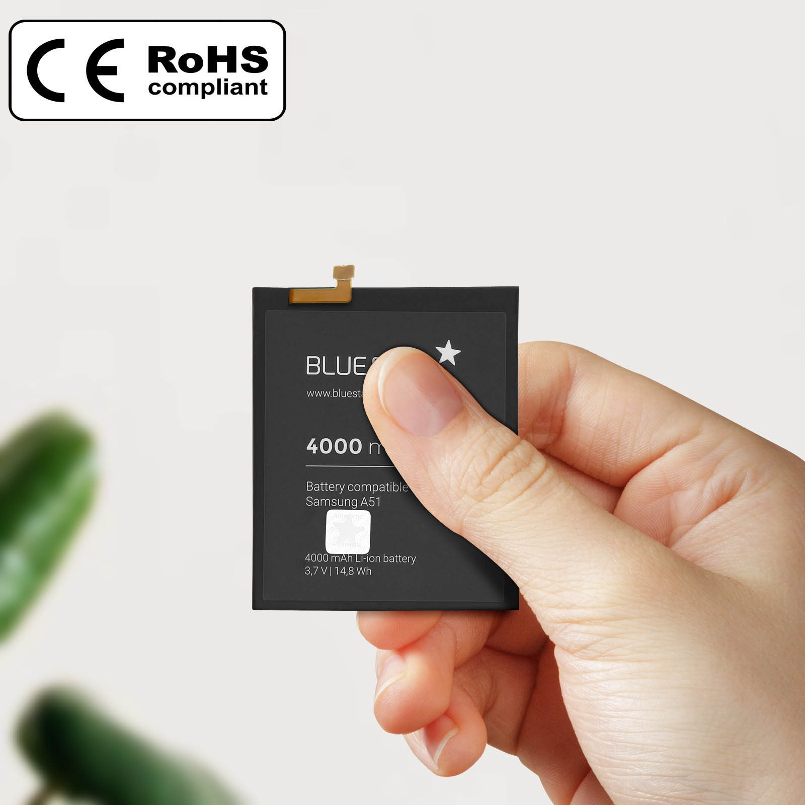 Una mano tiene una batteria di telefono nera. La batteria ha testo bianco e un connettore. È visibile un logo conforme a RoHS.