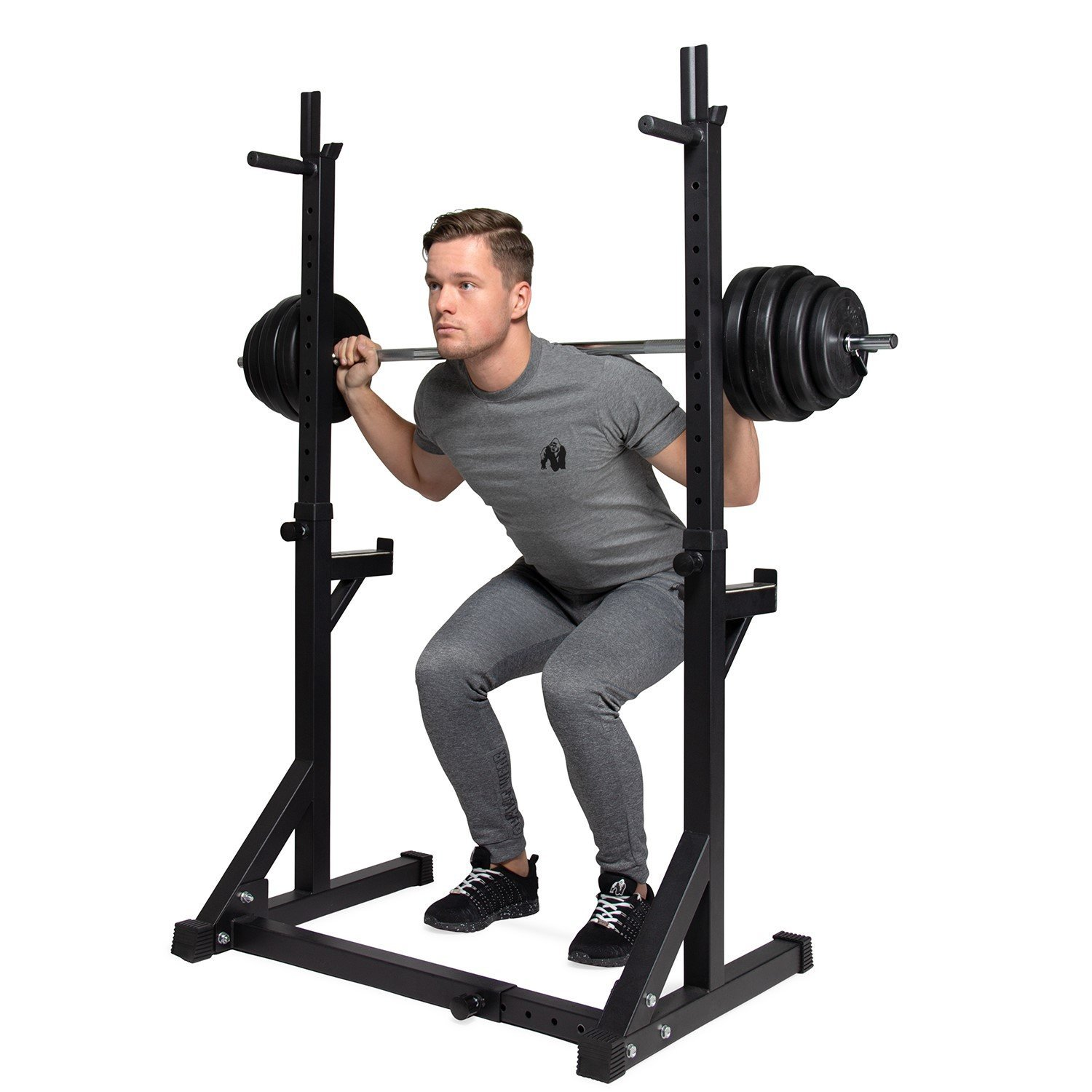 Ein Mann hockt mit einer Langhantel auf den Schultern. Er ist in einem Fitnessstudio und trägt graue Trainingskleidung. Hinter ihm steht ein schwarzes Squat-Rack.