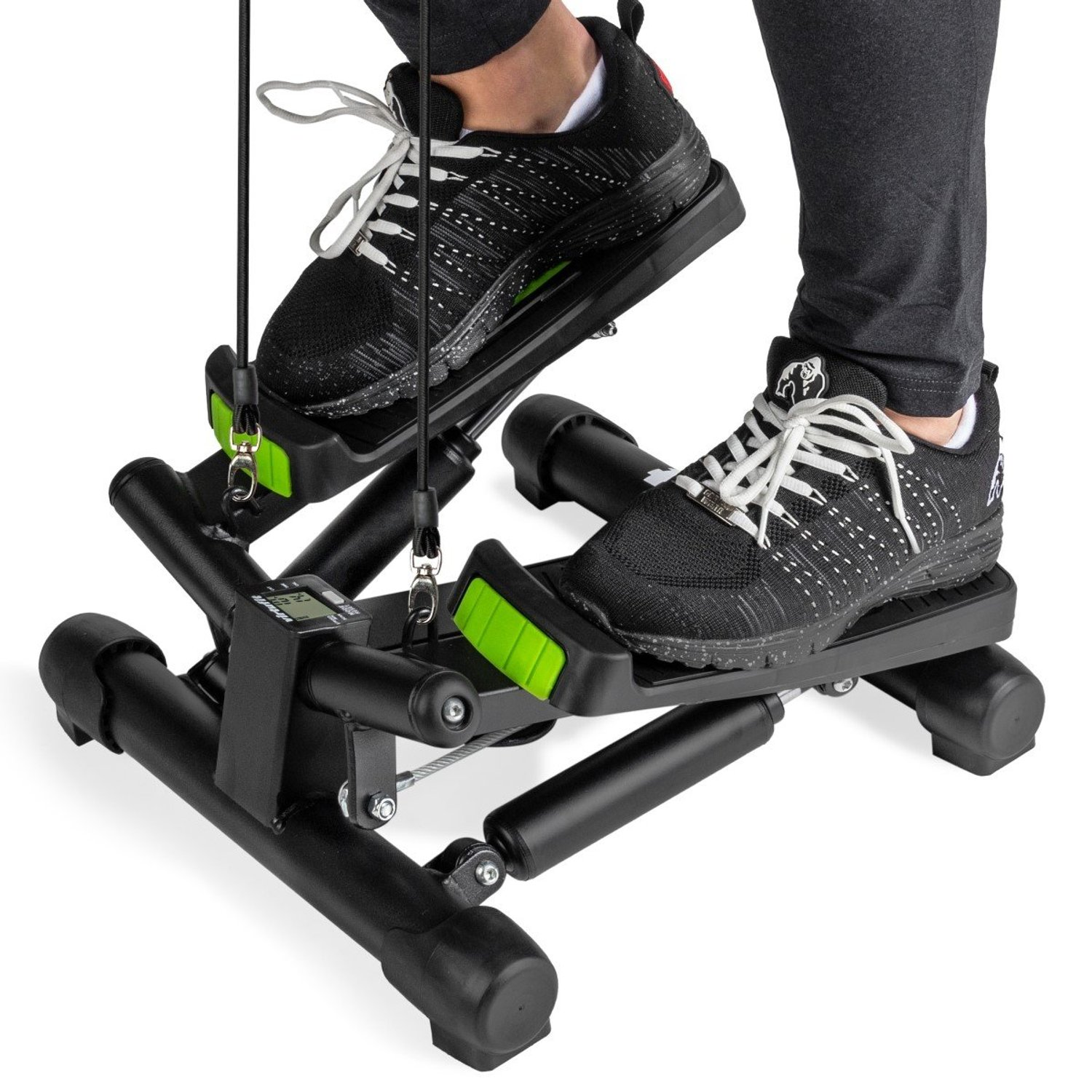 Person benutzt einen schwarzen Stepper mit schwarzen Schuhen, weißen Schnürsenkeln und grünen Akzenten. Der Stepper hat ein digitales Display. Der Hintergrund ist weiß.