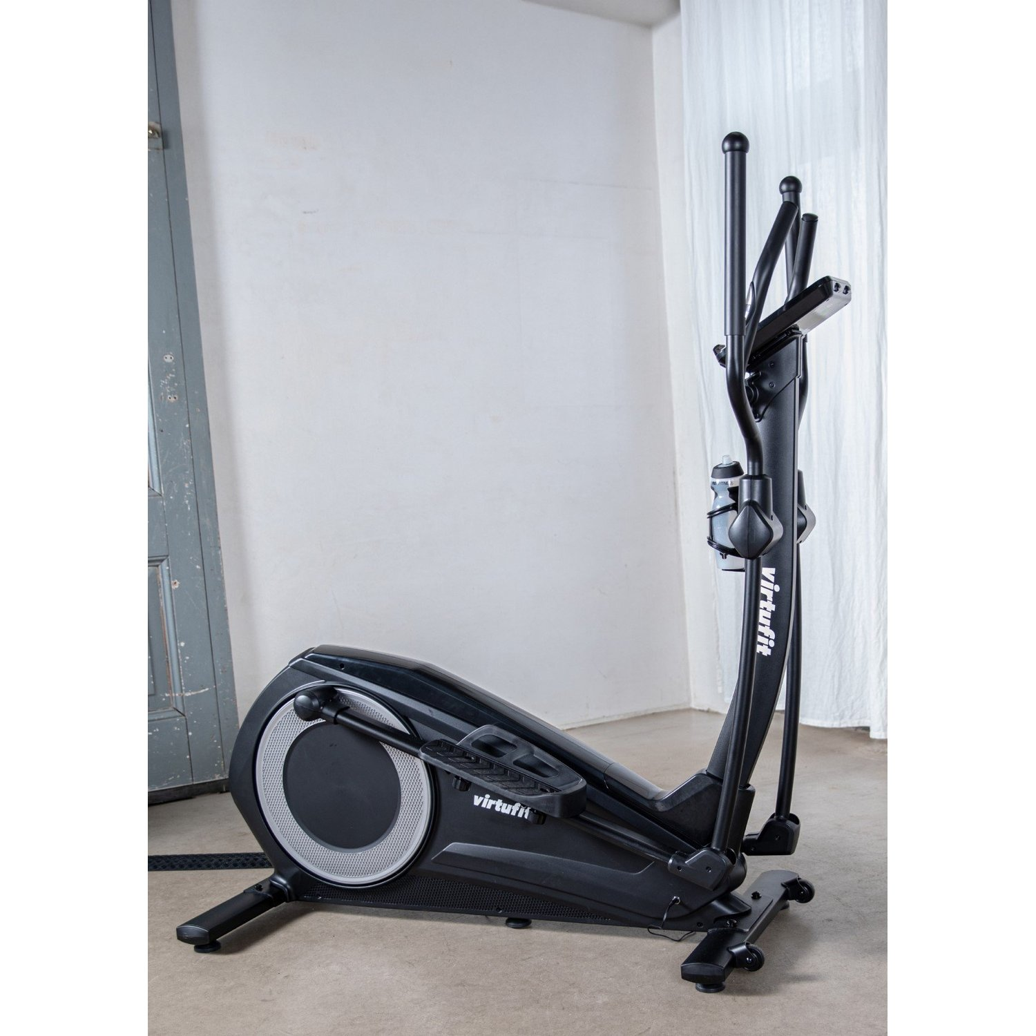 Eine schwarze Ellipsenmaschine der Marke Virtufit steht auf einem grauen Boden. Im Hintergrund eine weiße Wand, Tür und Vorhang.