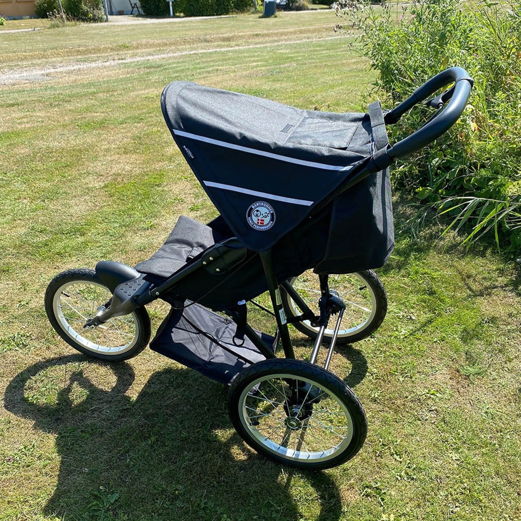 Ein schwarzer und silberner Jogging-Kinderwagen steht auf grünem Gras. Er hat drei Räder und ein schwarzes Verdeck.