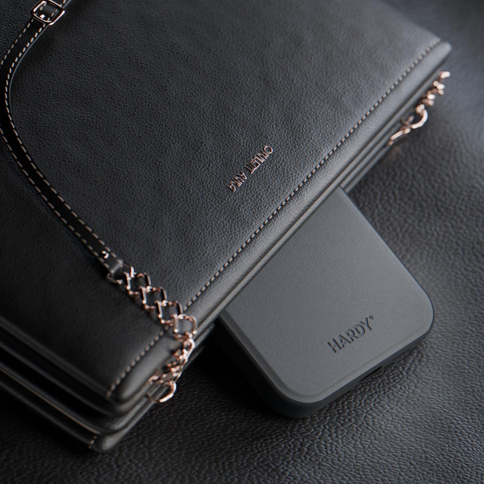 Borsa grigio scuro con catena dorata e telefono grigio all'interno. La borsa è su una superficie strutturata.