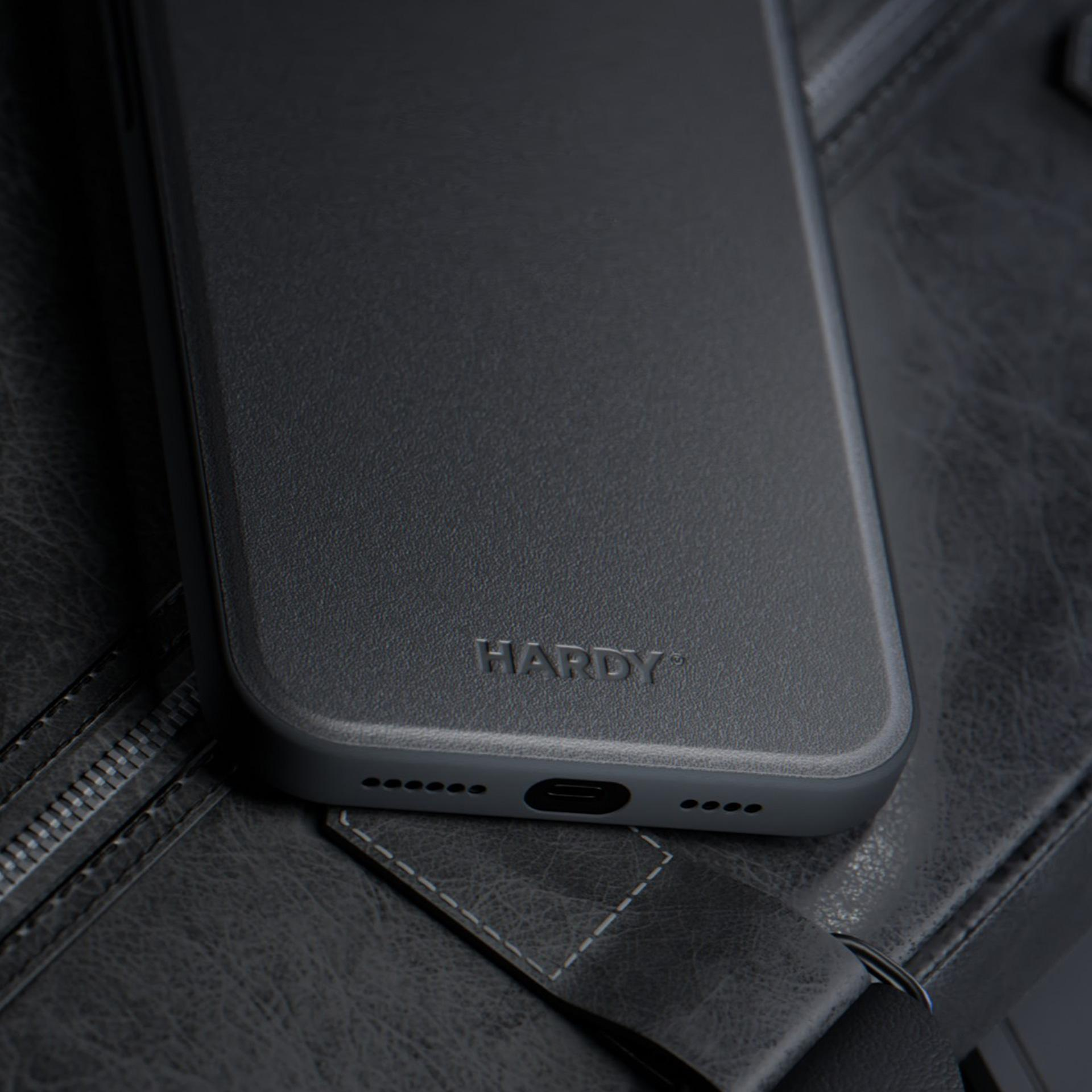 Una custodia grigia per telefono con 'HARDY' in rilievo poggia su una superficie in pelle grigio scuro strutturata.