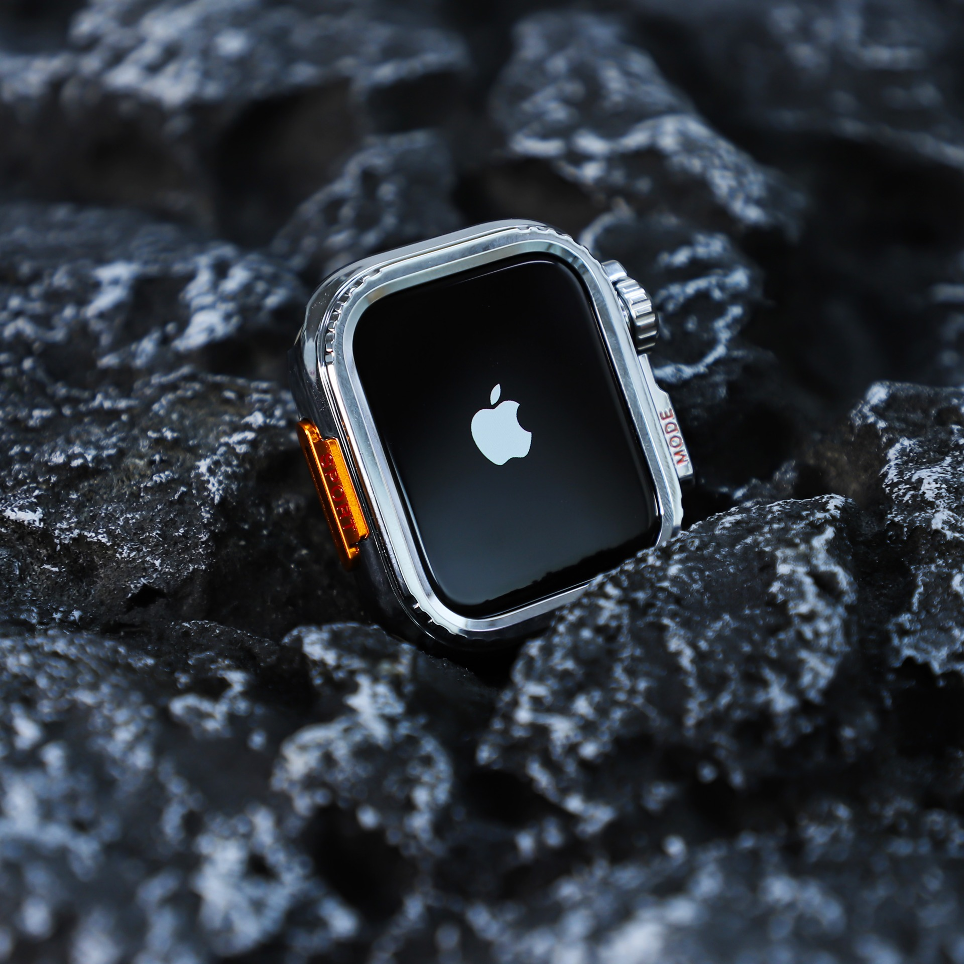 Apple Watch su rocce scure. L'orologio è argento con schermo nero e logo Apple. Dettagli arancioni.