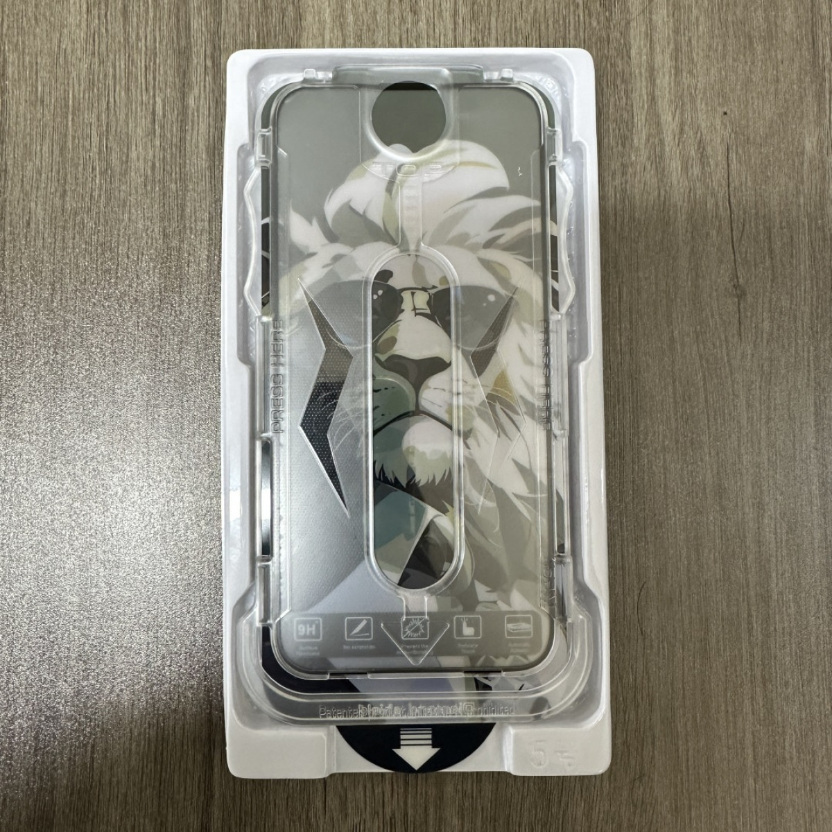Una custodia per telefono con un design a leone in una confezione di plastica trasparente su una superficie di legno. Il leone indossa occhiali da sole.
