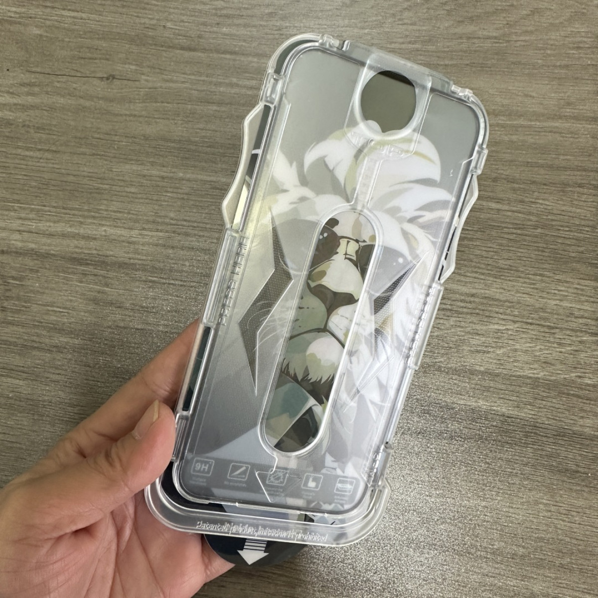 Una custodia trasparente per telefono con un design a leone tenuta in mano. Lo sfondo è una superficie di legno. La custodia è trasparente.
