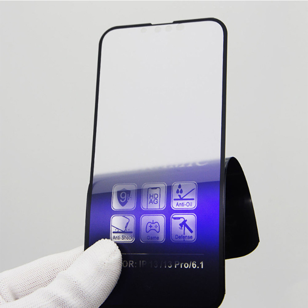 Un proteggi schermo per telefono è appoggiato su un supporto nero. Ha icone per antiurto, antiolio e altre funzioni. Una mano guantata lo tiene.