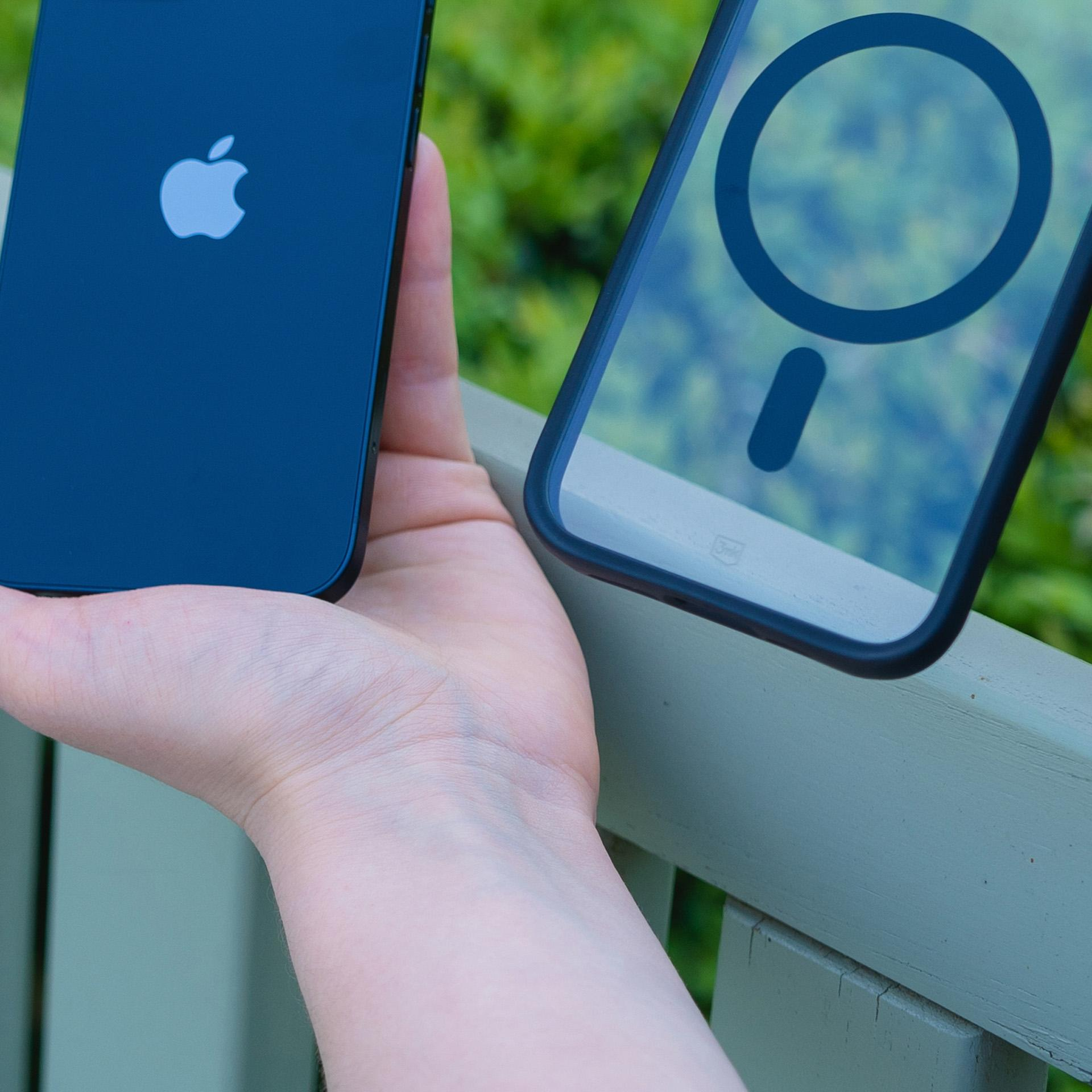 Dłoń trzyma niebieskiego iPhone'a i przezroczyste etui z okrągłym wzorem na zielonym tle.