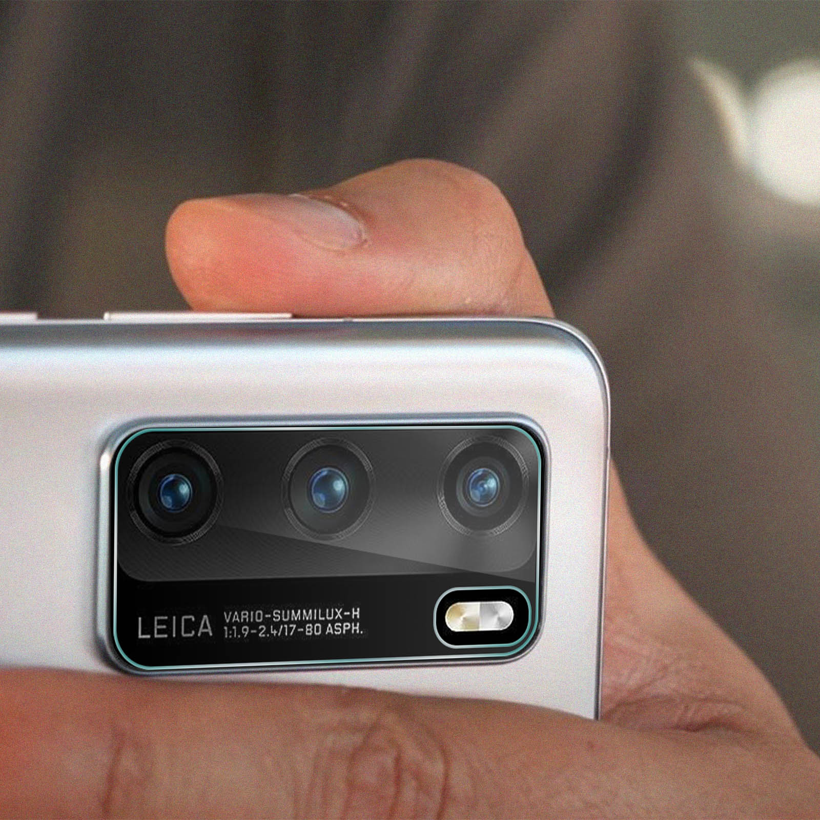 Primo piano di un telefono con tre obiettivi. Un dito tiene il telefono. Il marchio Leica è visibile.