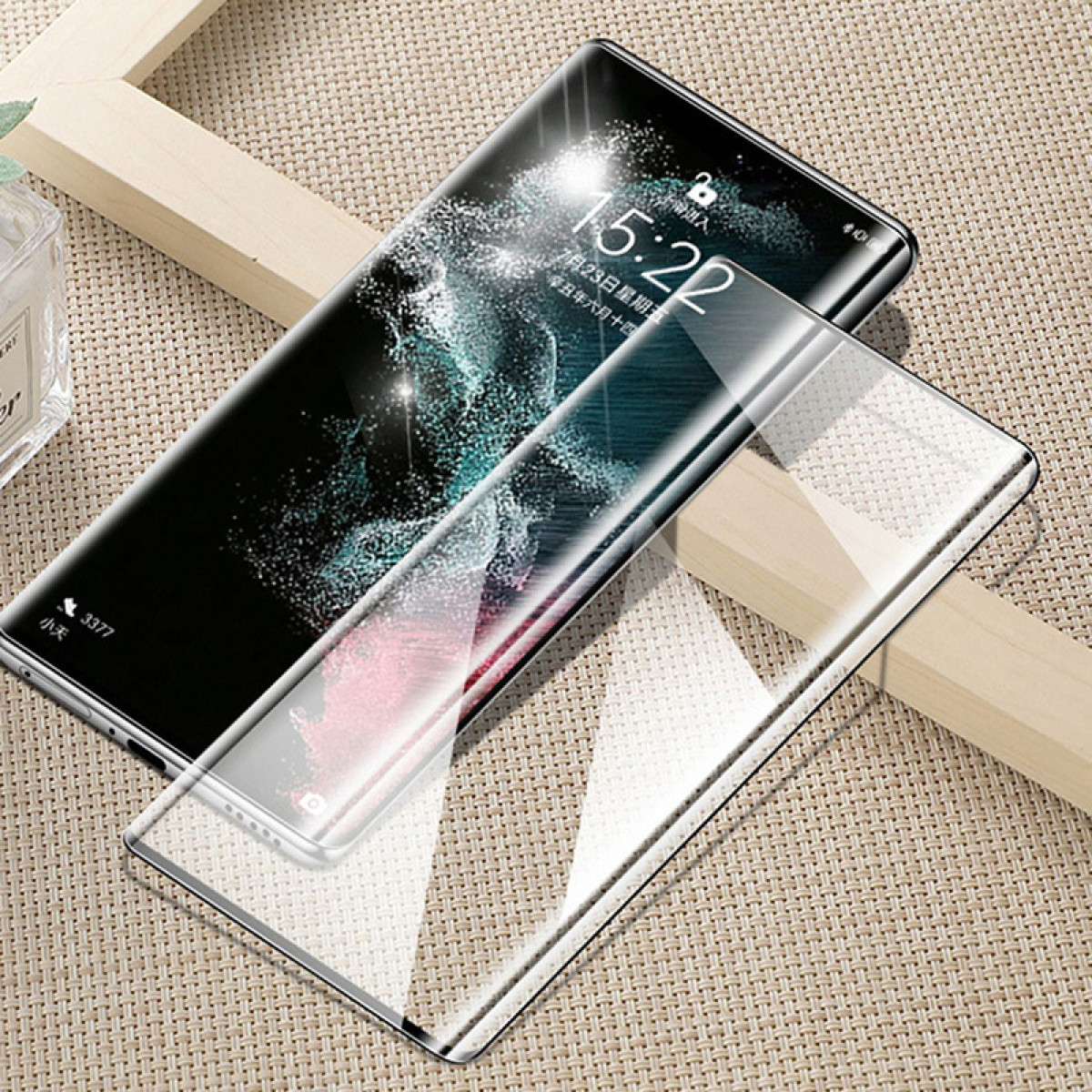 Uno smartphone con protezione schermo. Il telefono mostra le 15:22. Lo sfondo è una trama tessuta, con una cornice di legno.