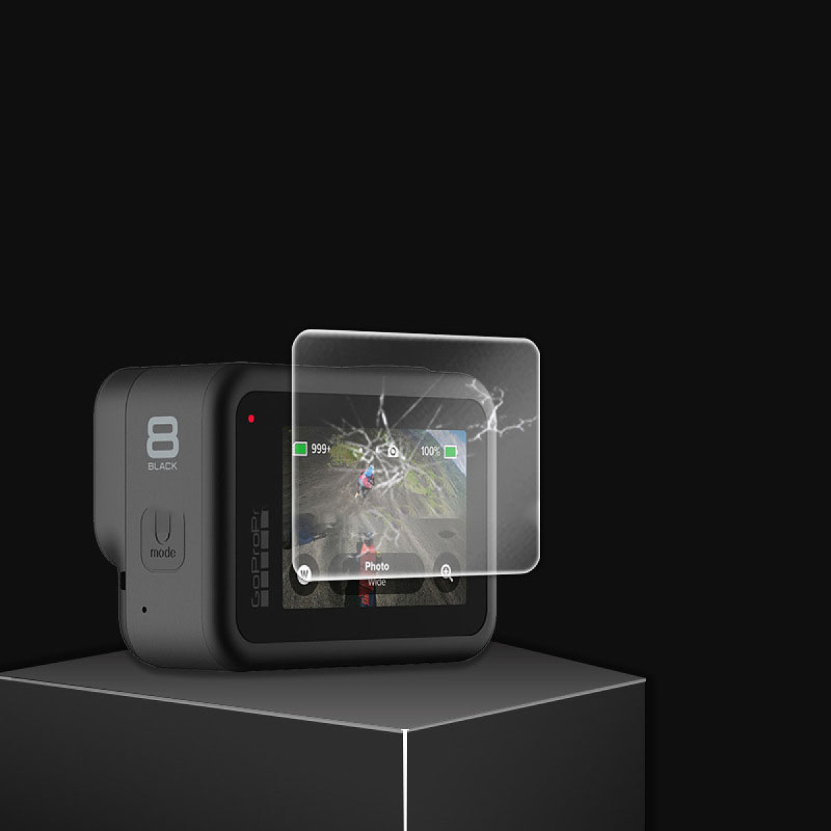 Fotocamera GoPro con protezione schermo rotta. Il display mostra un paesaggio. La fotocamera è su un supporto nero su sfondo nero.