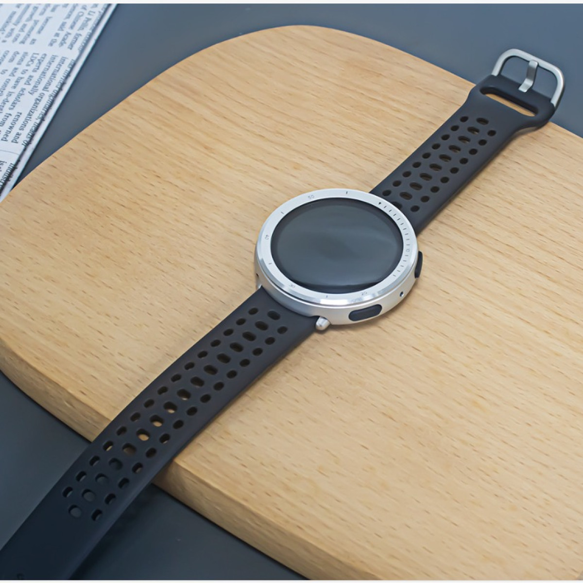 Uno smartwatch con cinturino nero è su una tavola di legno. L'orologio ha una lunetta argentata e uno schermo scuro.