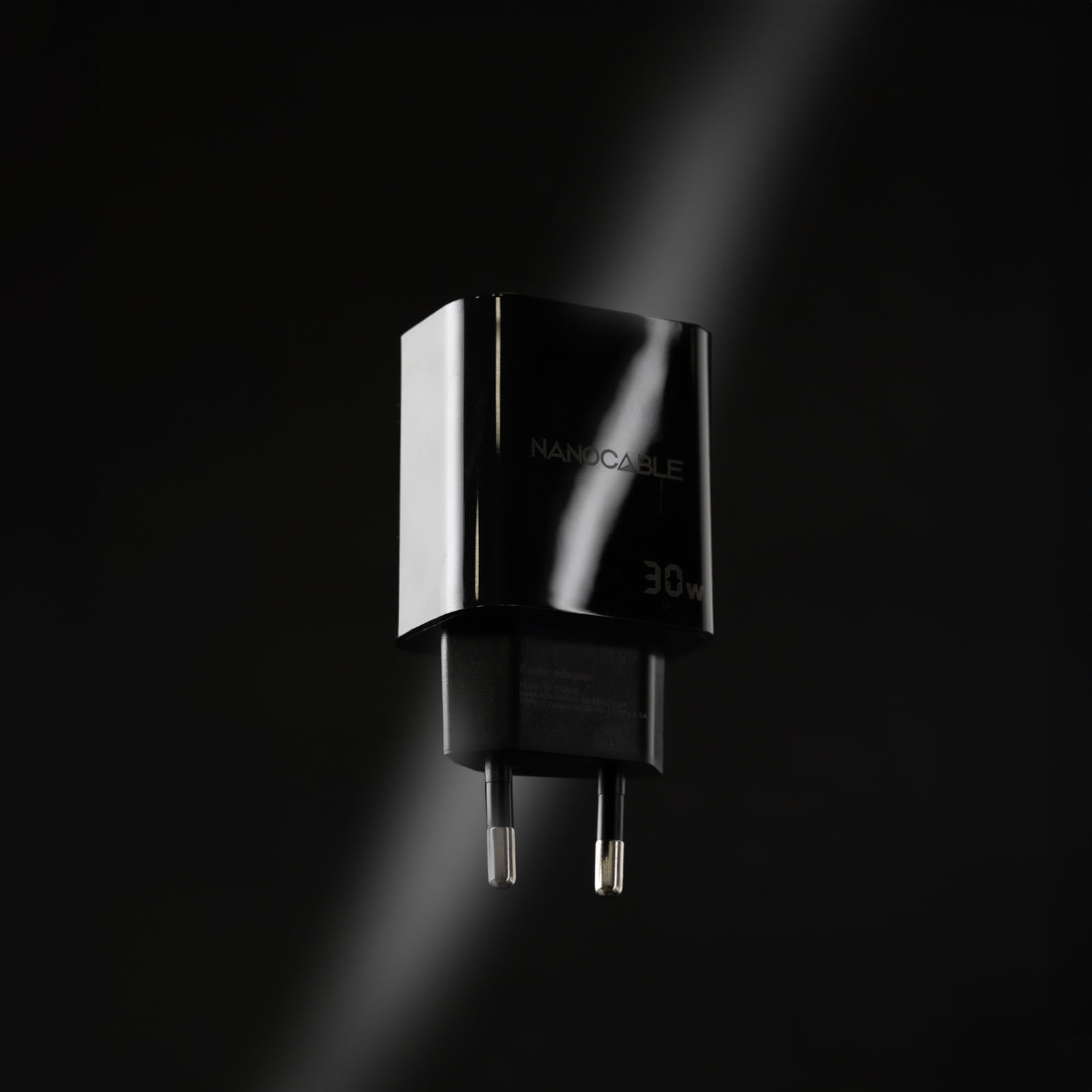Schwarzes Nanocable 30W-Ladegerät mit silbernen Stiften. Der Hintergrund ist ein dunkler Farbverlauf mit Lichtstrahl.